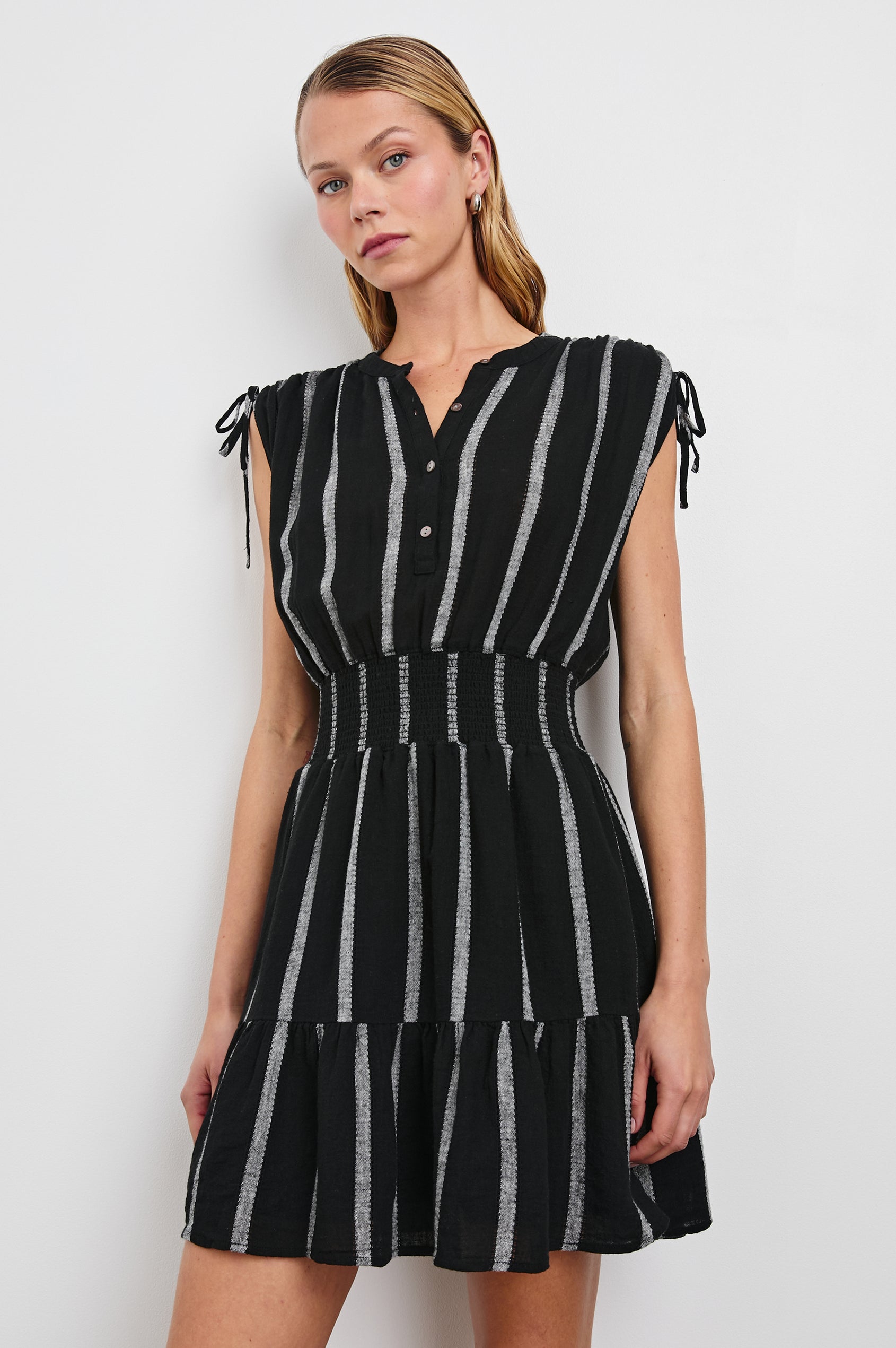 Samina Above-Knee Sleeveless Dress with drawstrings at the Arm Openings, Buttons along the Bodice, A Cinched Waist and a Tiered Skirt in Ash Leno Stripe Colorway, with Grey vertical stripes on black - Front View Featured on Model 