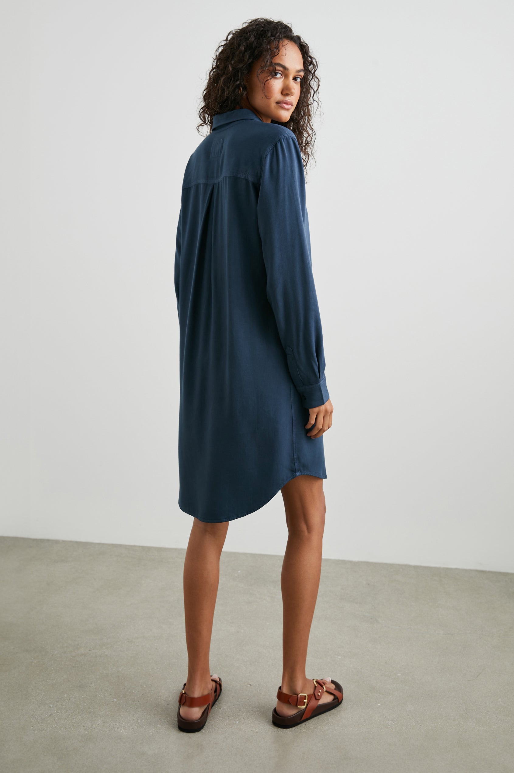 Sawyer Long-Sleeve Mini Dress with a Full Button Front, a Chest Patch Pocket, a Collar, Button Cuffs and a Low High Hem in Navy Colorway - Back Full Body View Featured on Model 