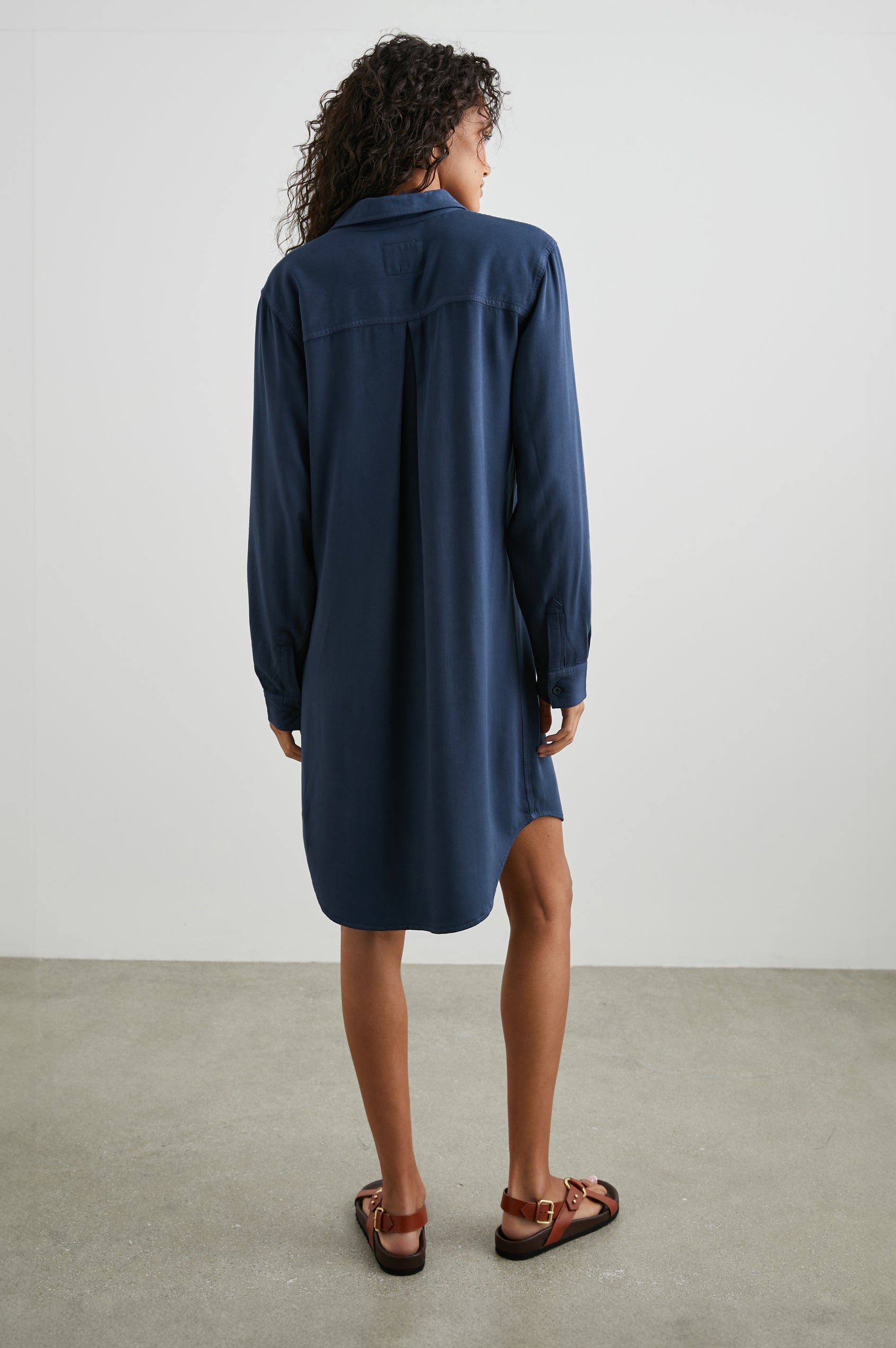 Sawyer Long-Sleeve Mini Dress with a Full Button Front, a Chest Patch Pocket, a Collar, Button Cuffs and a Low High Hem in Navy Colorway - Back Full Body View Featured on Model 