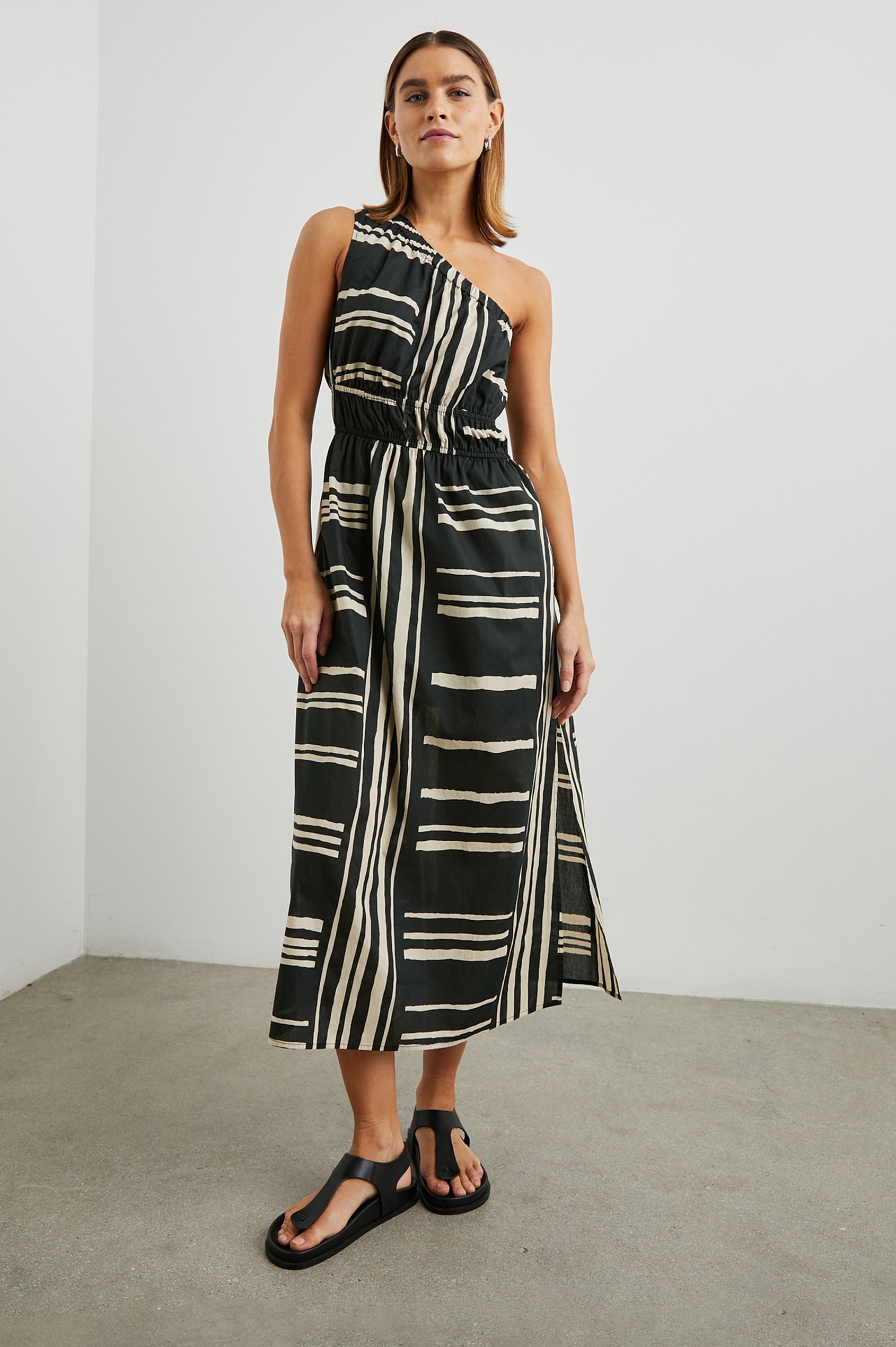 Selani Midi Dress With an Asymmetrical Neckline, Mid-Thigh Slide Slit and Cinched Waistband in Island Stripe Colorway, with alternating white and black horizontal and vertical stripes - Front Full Body View Featured on Model