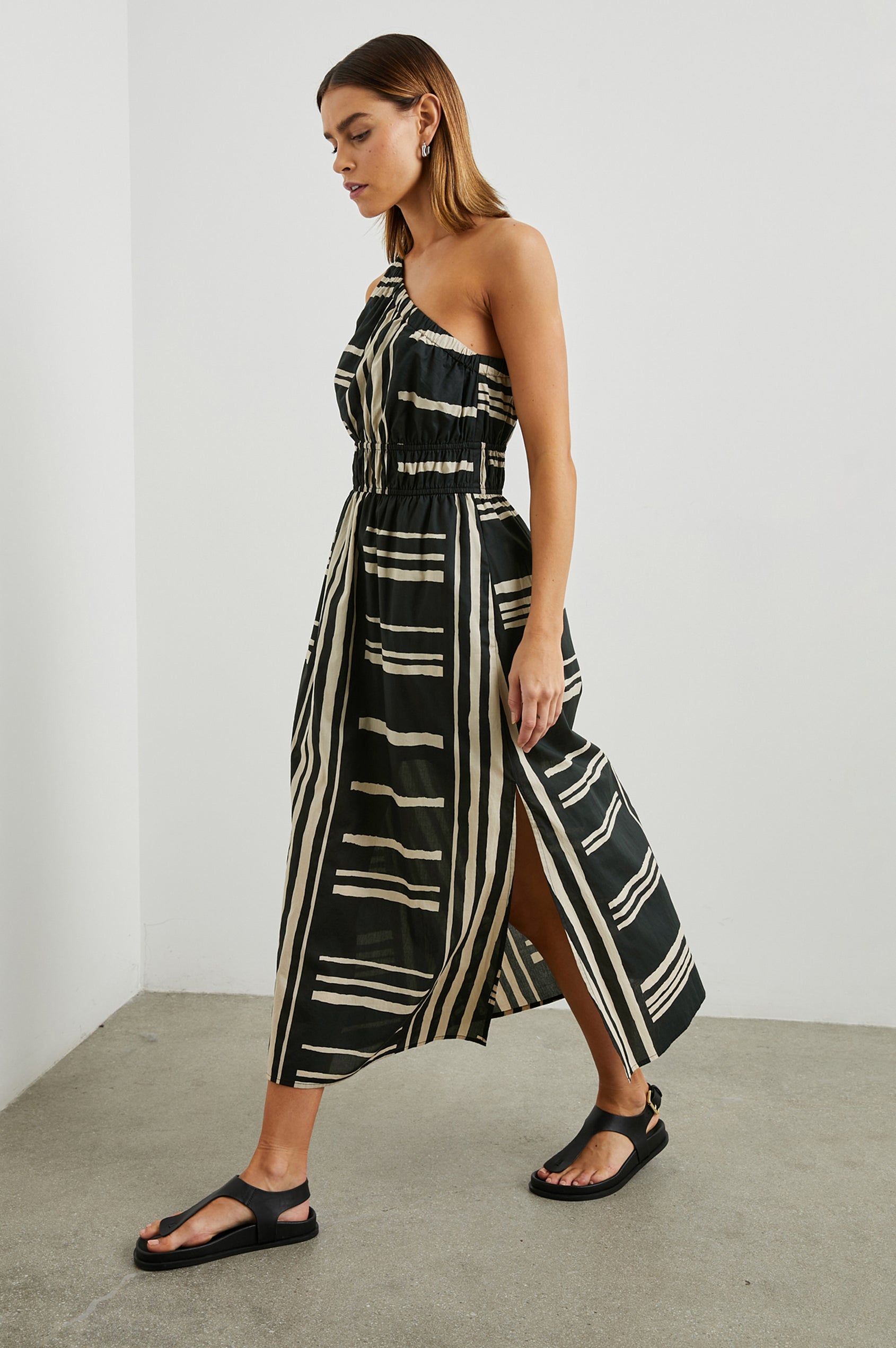 Selani Midi Dress With an Asymmetrical Neckline, Mid-Thigh Slide Slit and Cinched Waistband in Island Stripe Colorway, with alternating white and black horizontal and vertical stripes - Side Full Body View Featured on Model