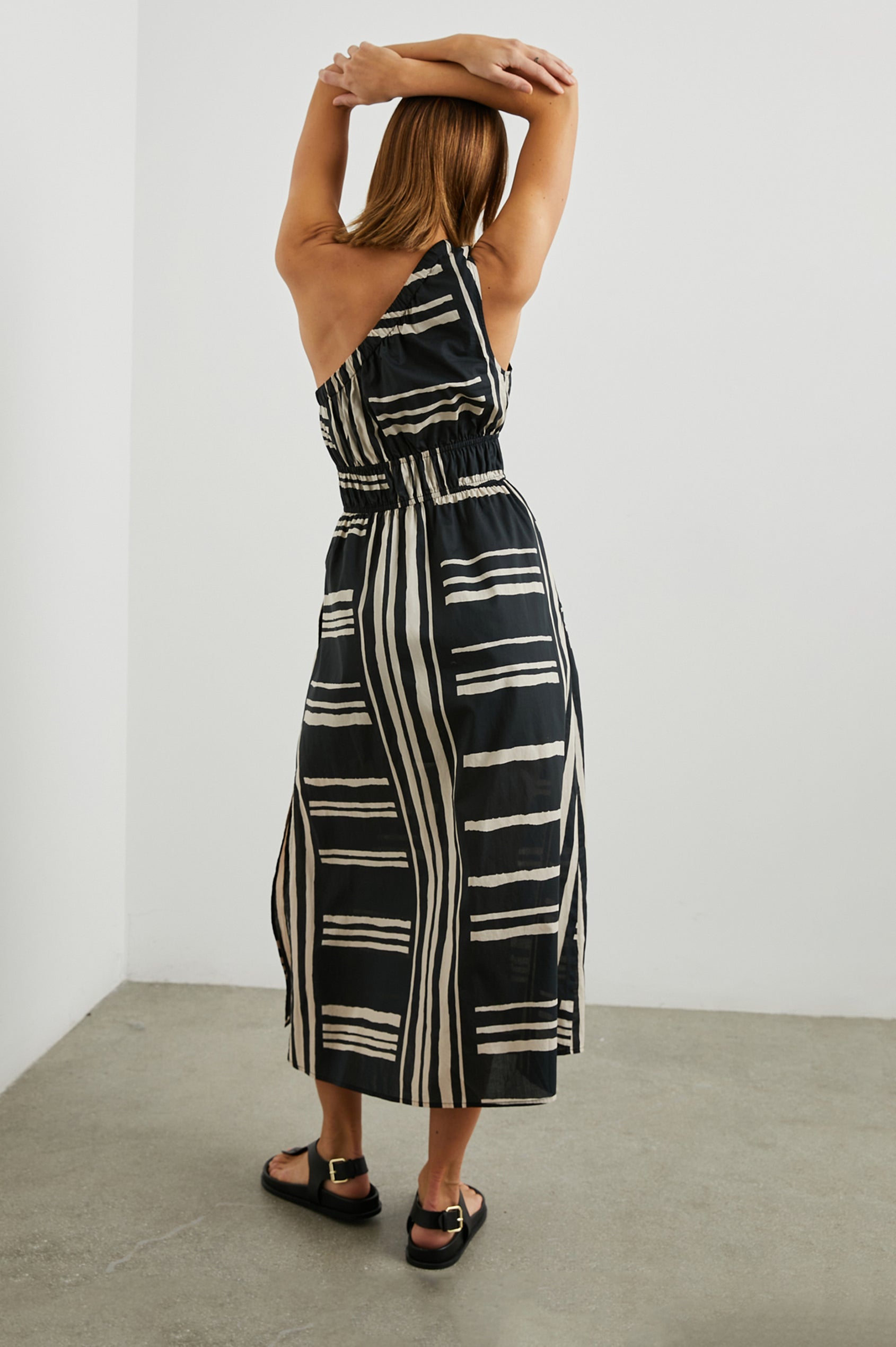 Selani Midi Dress With an Asymmetrical Neckline, Mid-Thigh Slide Slit and Cinched Waistband in Island Stripe Colorway, with alternating white and black horizontal and vertical stripes - Back Full Body View Featured on Model