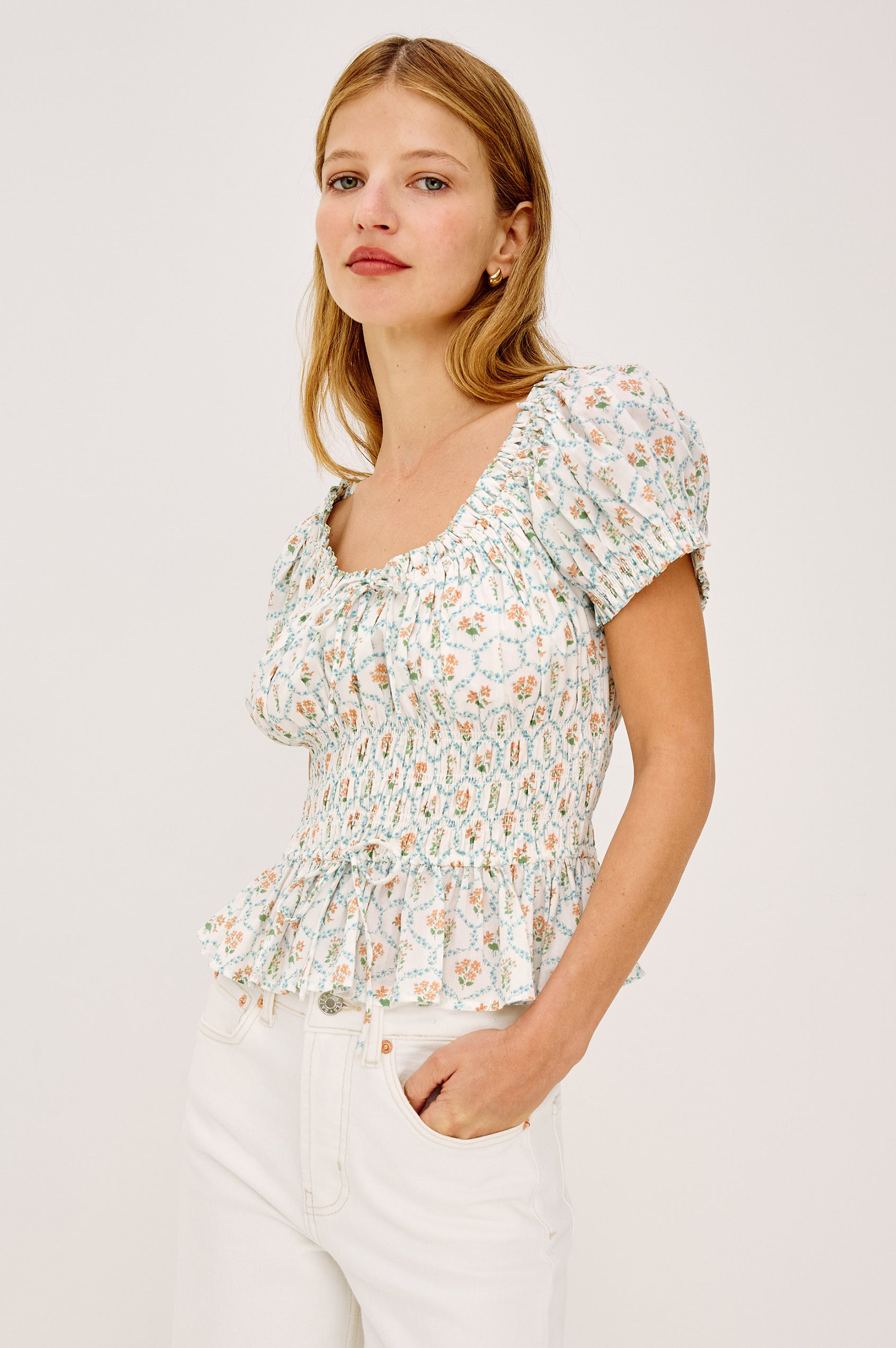 Serena Crop Top in Beach Cotton With Scoop Neckline, Short Puff Sleeves, Center-Front Ties, Smocked Waist, and Flared Peplum Hem in Peach Peony Colorway - Upper Body Front View Featured on Model