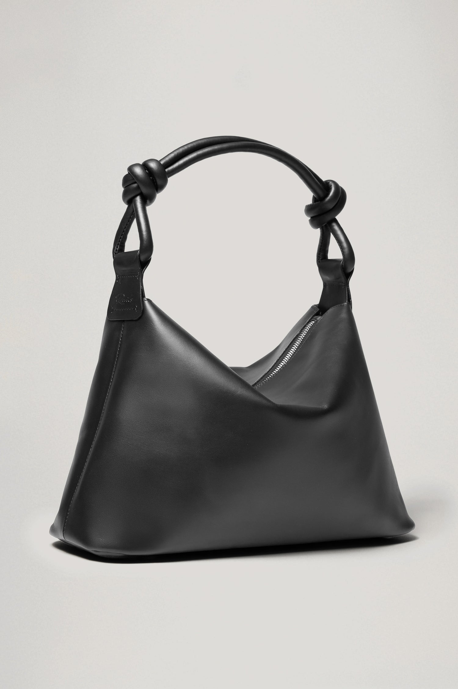 The Siena is a true slouchy hobo bag, crafted from smooth leather with a knotted top strap and a zip closure finished with a fringed tassel. In Black Leather Colorway. Front view featured.
