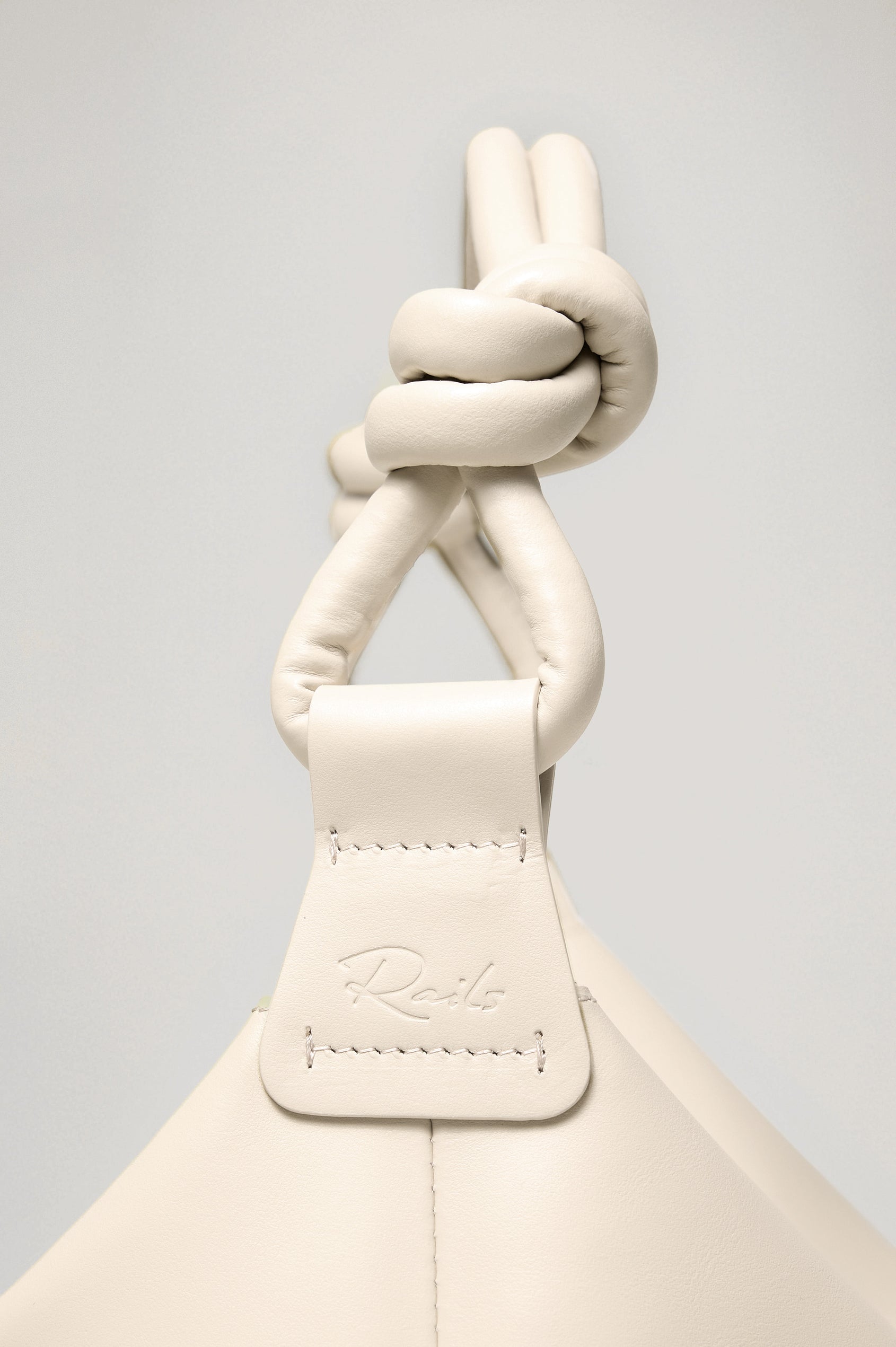 The Siena is a true slouchy hobo bag, crafted from smooth leather with a knotted top strap and a zip closure finished with a fringed tassel. In Bone Leather Colorway. Detailed view of strap featured.