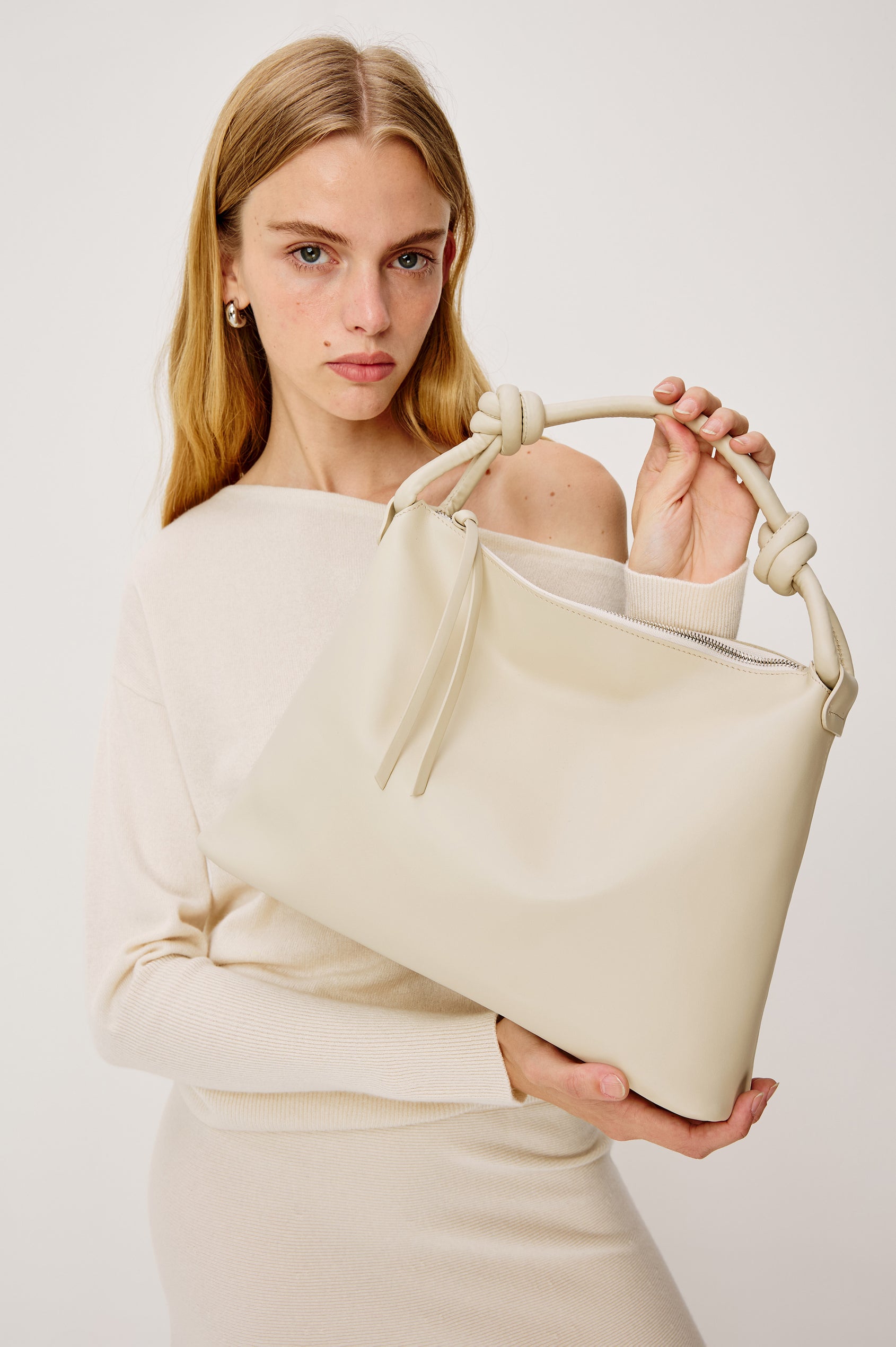The Siena is a true slouchy hobo bag, crafted from smooth leather with a knotted top strap and a zip closure finished with a fringed tassel. In Bone Leather Colorway. Full body side view featured on model.