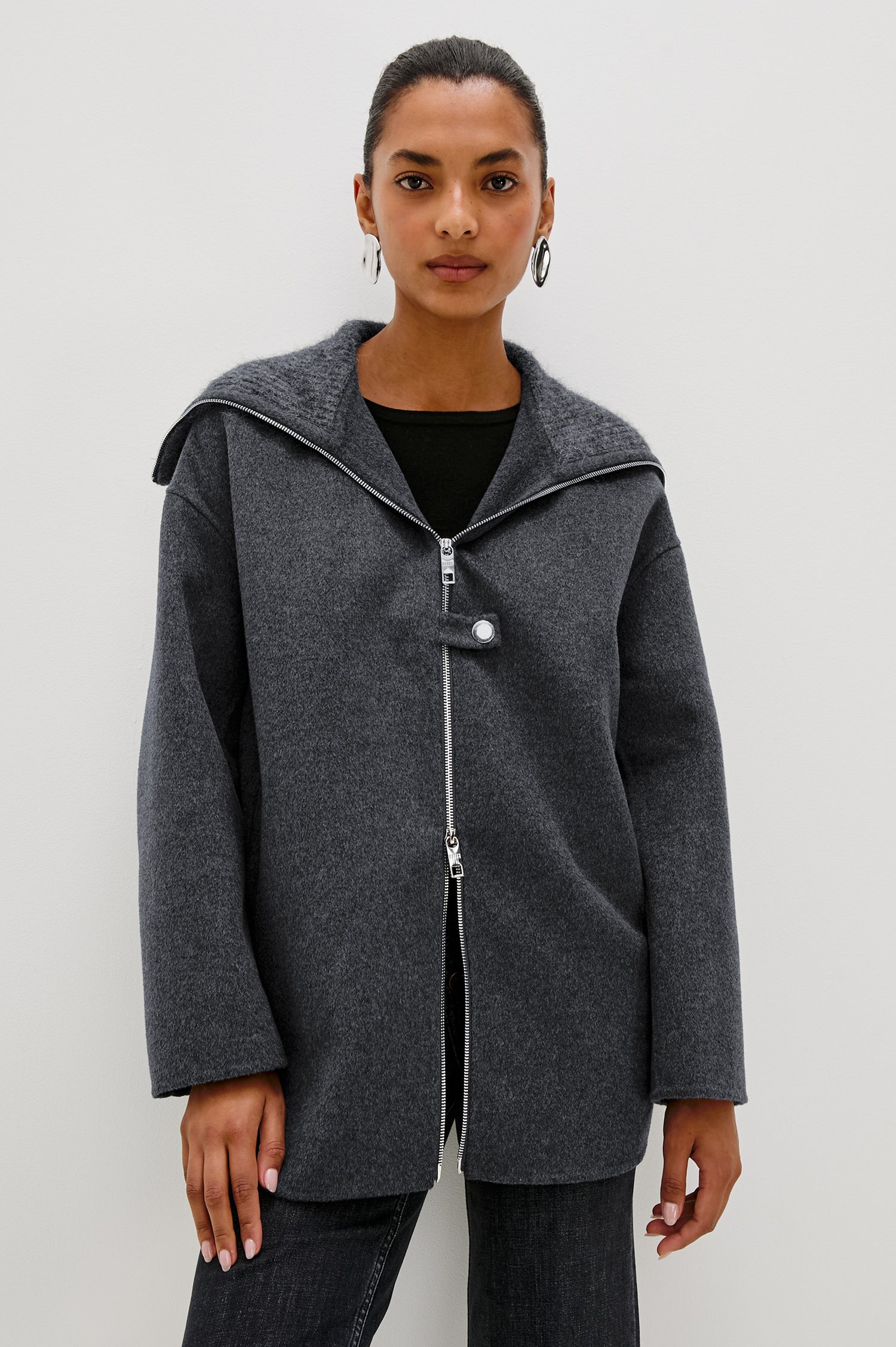 Silves is a heavyweight wool blend long jacket with a spread collar and slightly boxy fit. Slit pockets and a button details in charcoal color. Front view featured on model.