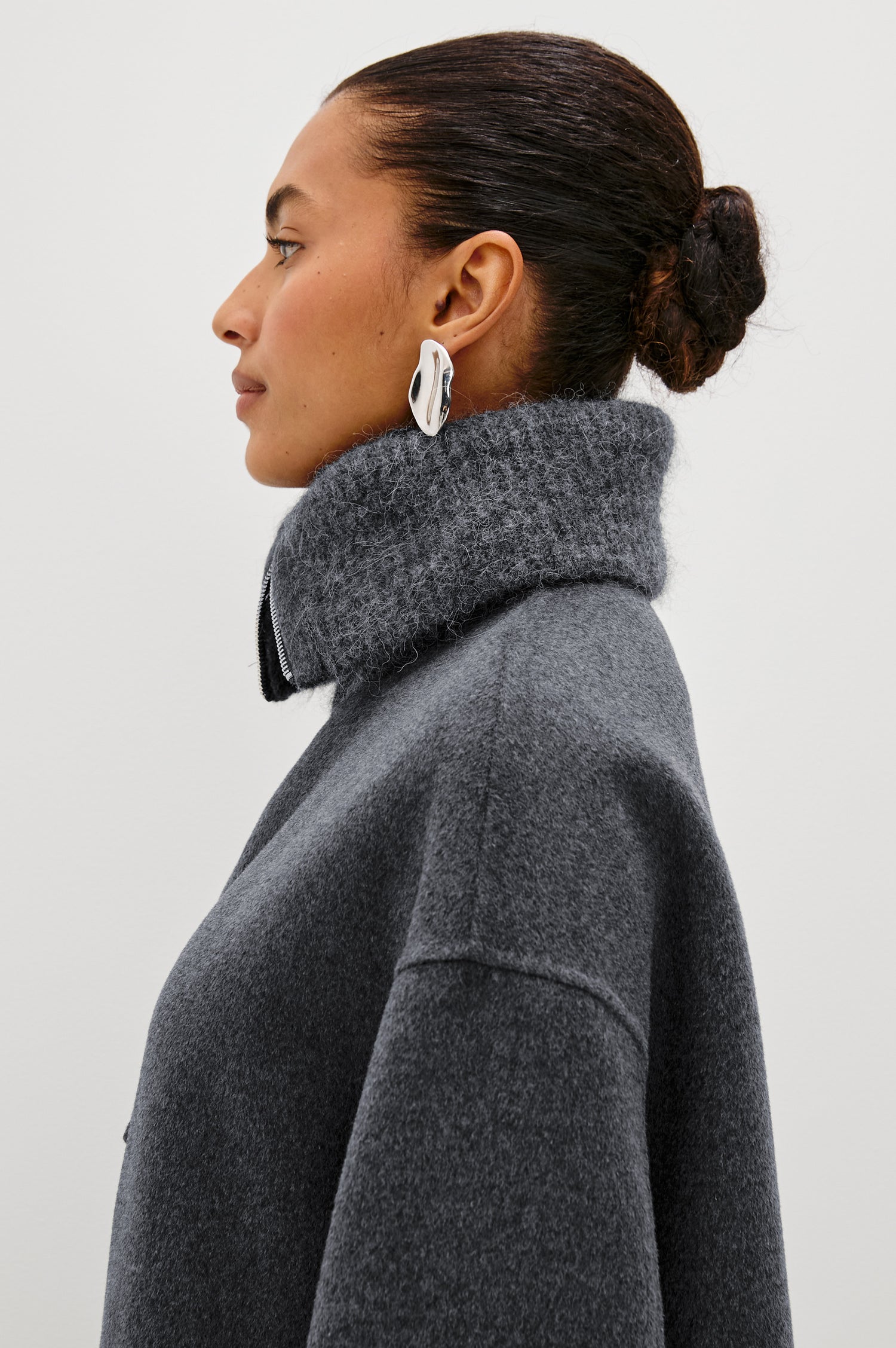 Silves is a heavyweight wool blend long jacket with a spread collar and slightly boxy fit. Slit pockets and a button details in charcoal color. Close up side view featured on model.