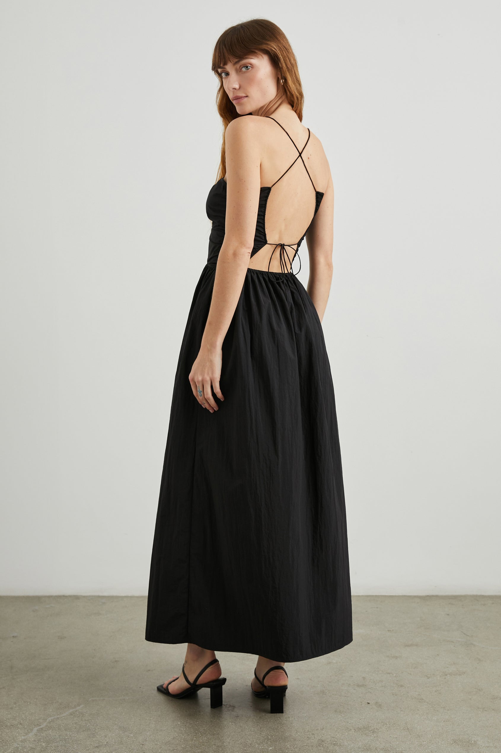 Silvia Sleeveless Maxi Dress with Spaghetti Straps with a Lower Back Tie, an Open Back, and Cutouts Along the Center of the Bodice in Black Nylon Colorway - Back Full Body View Featured on Model