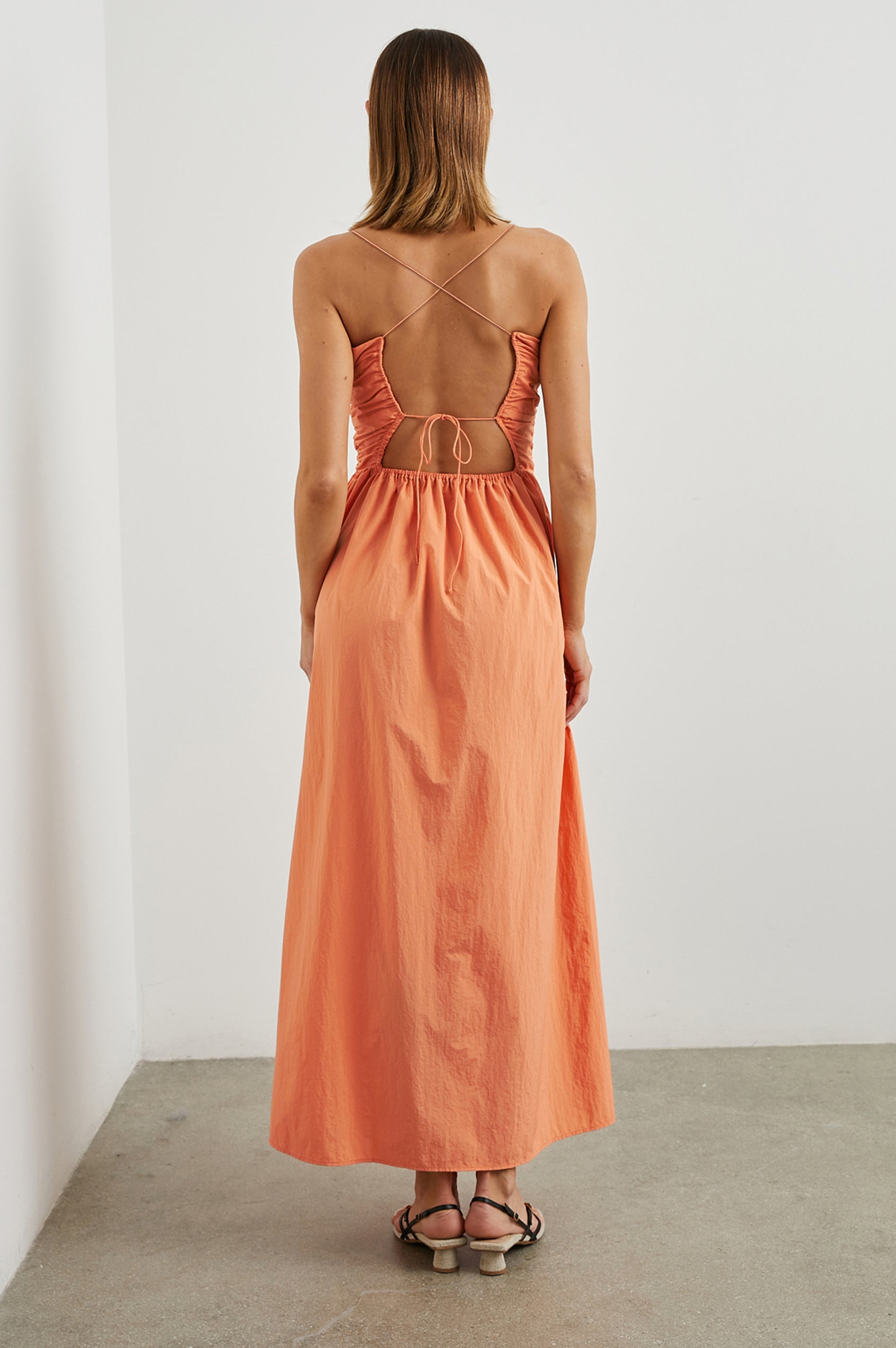 Silvia Sleeveless Maxi Dress with Spaghetti Straps with a Lower Back Tie, an Open Back, and Cutouts Along the Center of the Bodice in Papaya Colorway - Back Full Body View Featured on Model