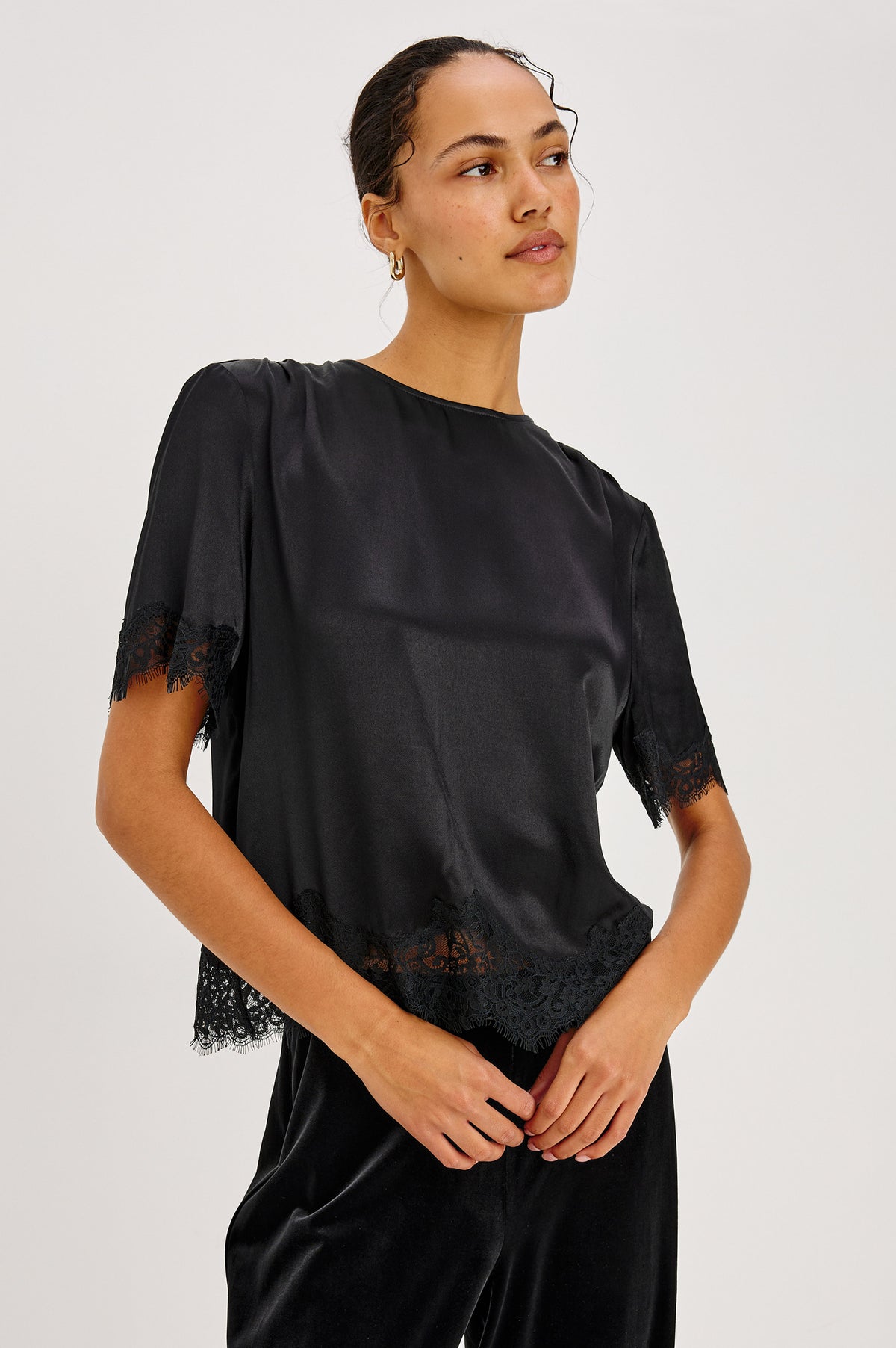 Sonora Shirt in Satin Crepe With Crew Neckline, Loose Boxy Fit, Shirred Shoulders, Short Sleeves, Button-Loop Back Keyhole, and Lace Trim in Black Colorway - Upper Body Front View Featured on Model