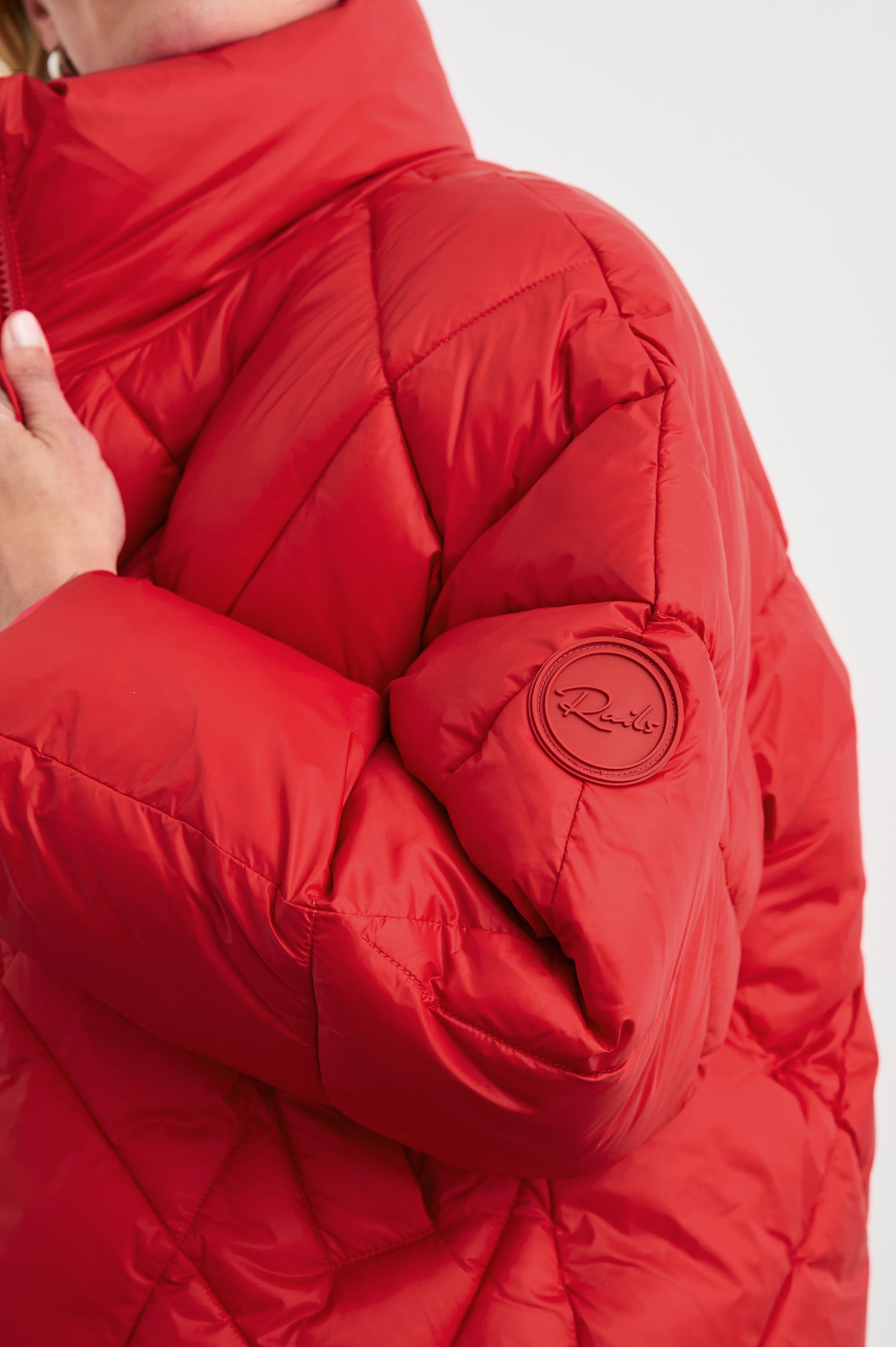 Summit Cropped Puffer Jacket with a Mid-Neck Collar, Two Pockets and a Rails Logo on the Arm in Scarlet Colorway - Side View Featured on Model
