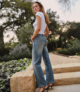 Woman wearing a white baby tee with denim jeans and black heels in a garden setting.