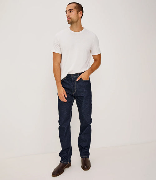 Man wearing a white t-shirt and dark jeans on a plain background