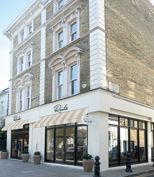 A street-facing retail storefront on a brick building corner with large glass windows, cream-colored facade, striped awnings, and the word 'Rustics' visible above the entrances.