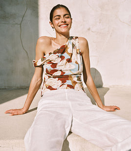 Woman wearing a floral top and white pants sitting on a stone surface.