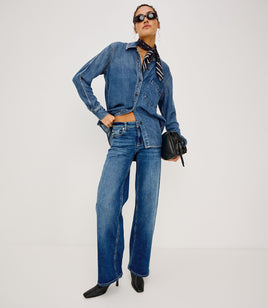 Woman wearing a blue denim outfit with sunglasses and a black handbag on a white background