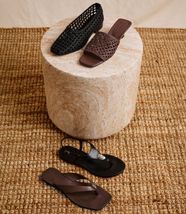 Two pairs of shoes on a round stone surface and two shoes on a textured beige rug.