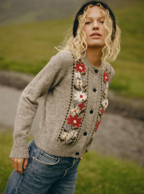 Woman wearing a grey floral sweater with blue jeans and a black cashmere beanie.