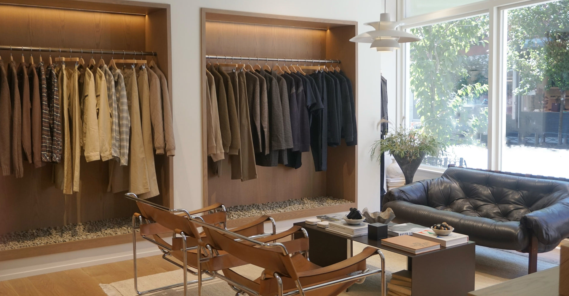 Modern interior with clothing racks, chairs, and a sofa near large windows.