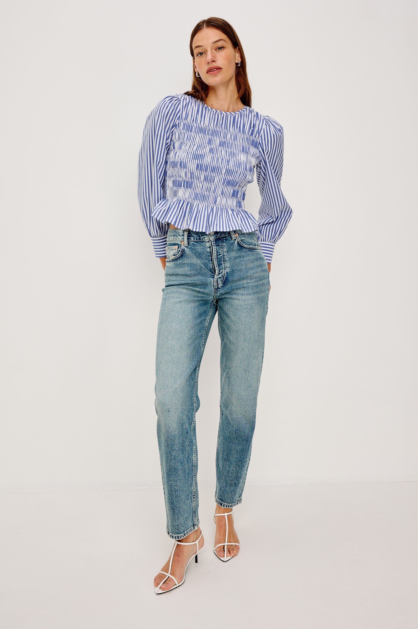 Tabi is a long sleeve crew neck top with puff sleeves and buttons at cuff, the bodice is pleated with a peplum hem in a blue Mariner White Stripe colorway. Front full body view featured on model.