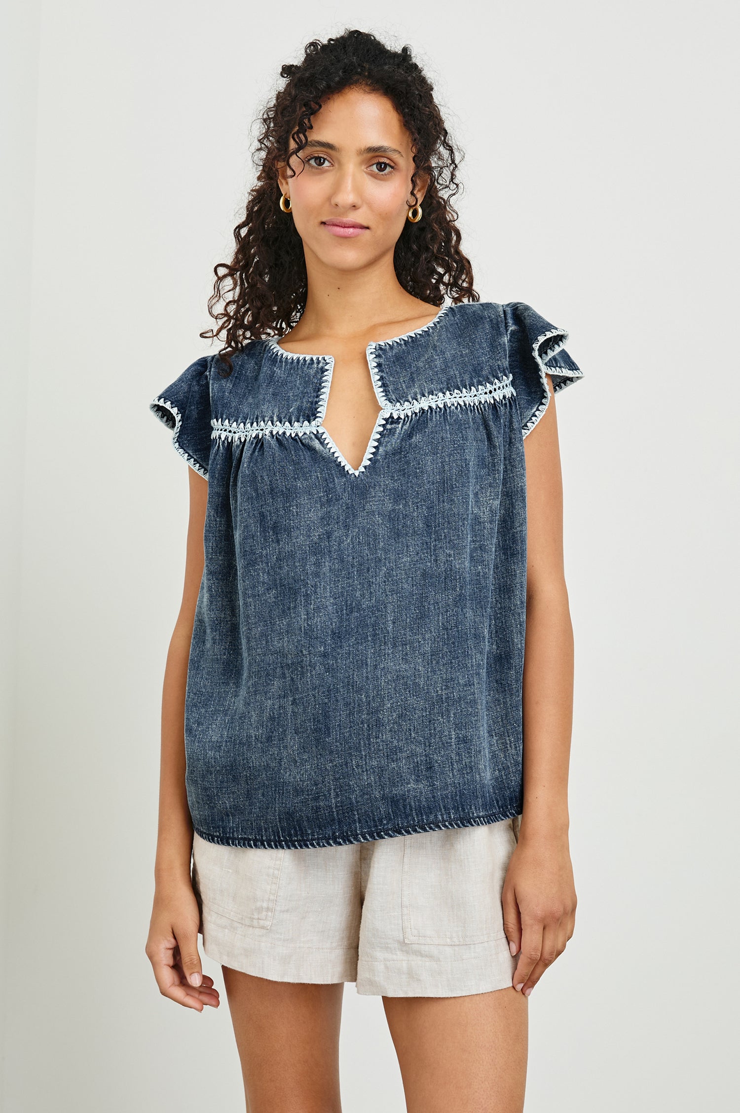 Tafia Top with an Open V-neck, Short Ruffle Cap Sleeves, and a White Blanket Stich along the Neckline, Cuffs and Yoke Seam in Classic Blue Colorway - Front Untucked View Featured on Model