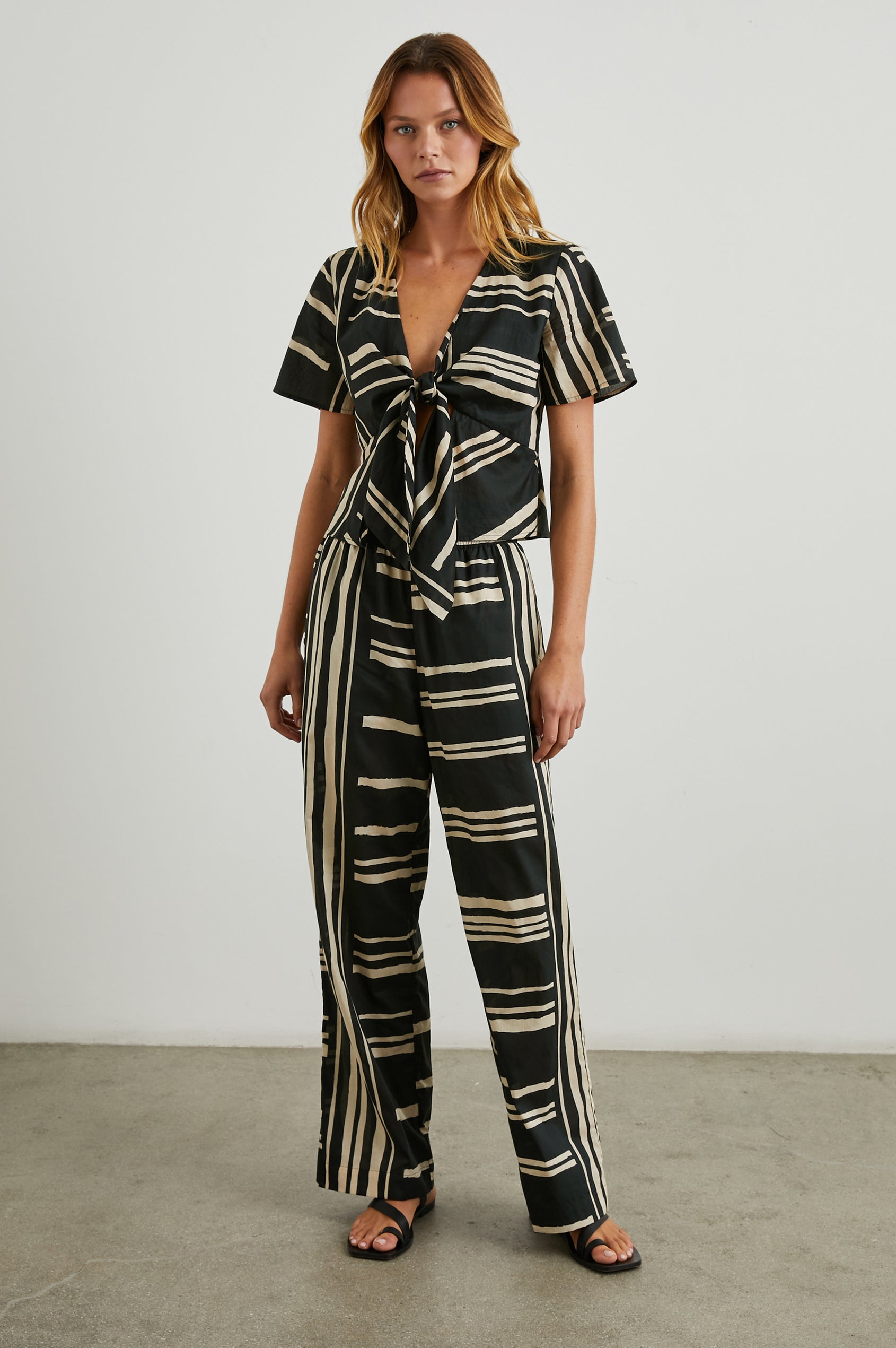 Tia Short-Sleeve Top Closed with a Front Tie and a Deep V Neck in Island Stripe Colorway, Cream Horizontal and Vertical Stripes on Black - Front Full Body View Featured on Model