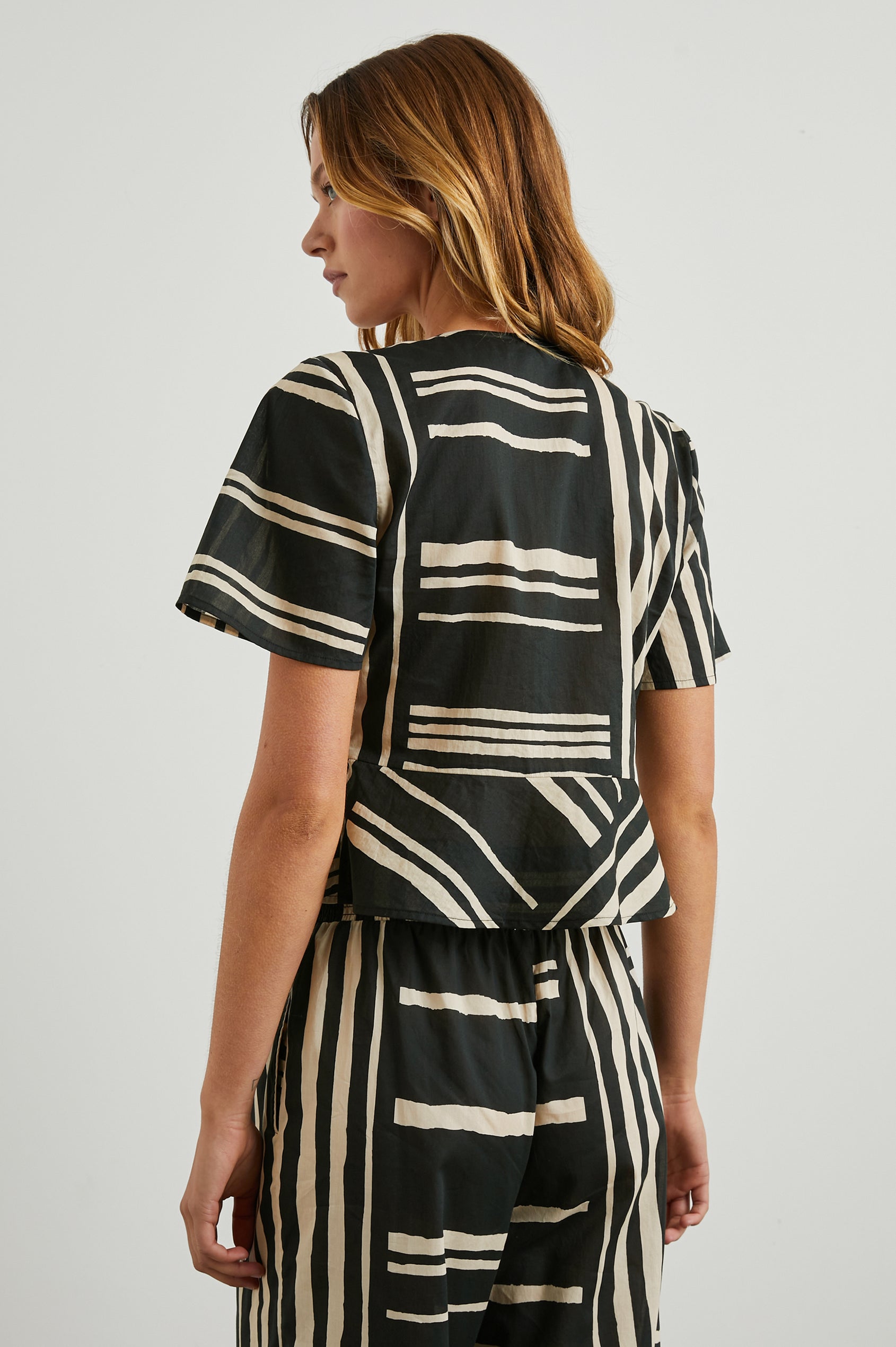 Tia Short-Sleeve Top Closed with a Front Tie and a Deep V Neck in Island Stripe Colorway, Cream Horizontal and Vertical Stripes on Black - Back View Featured on Model