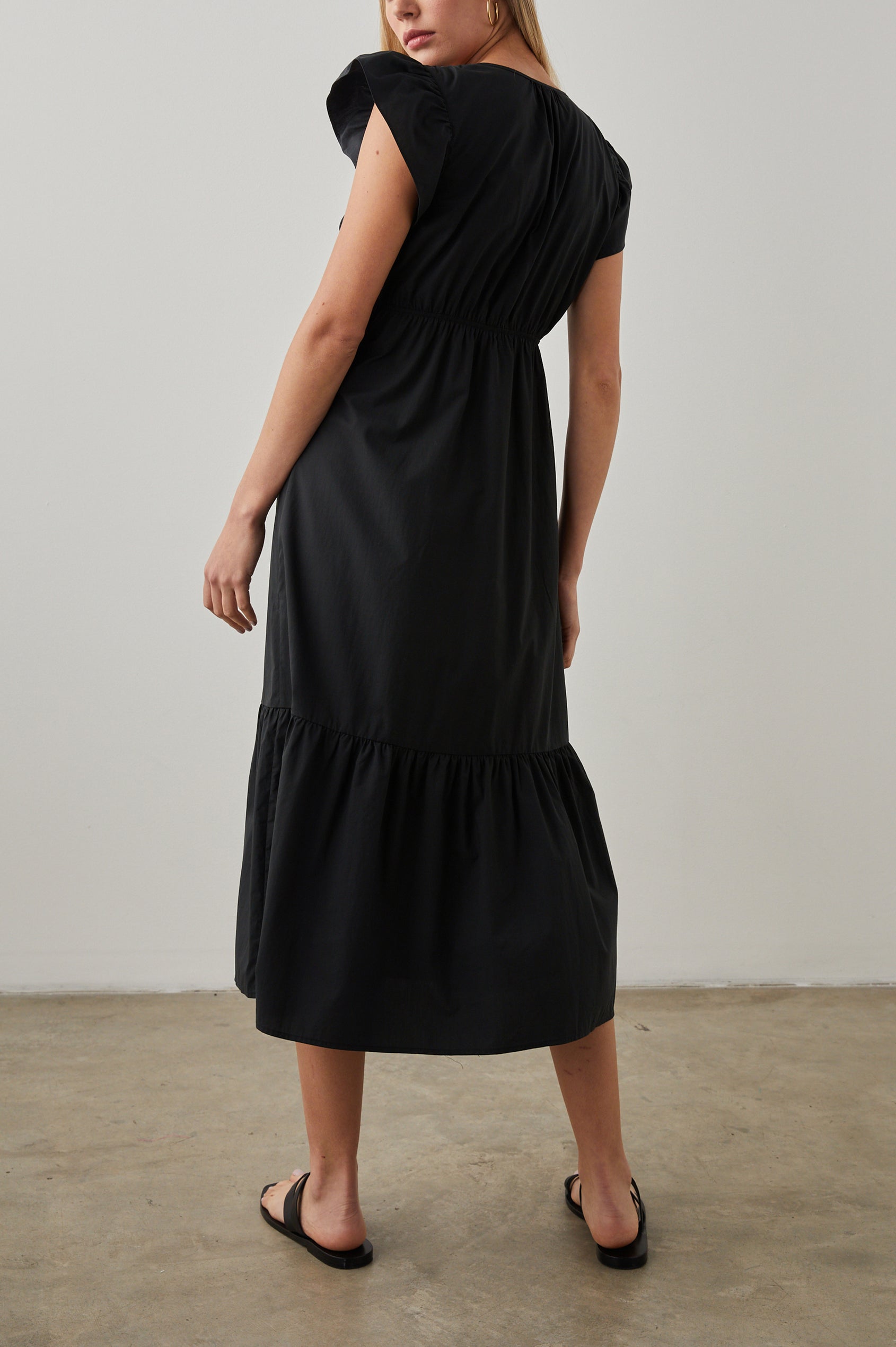 Tina Short Sleeve Midi Dress with Flutter Sleeves, a Deep V Neck with a Cutout and a Tiered Skirt in Black Colorway - Back Full Body View Featured on Model 