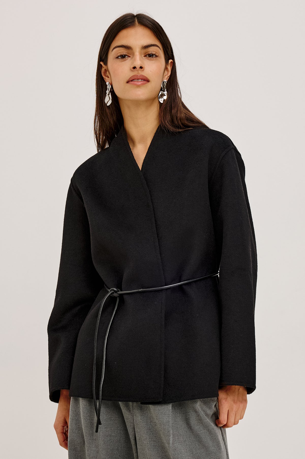 Tokyo Jacket in Wool Blend With Collarless Neckline, Leather Belt Ties, Long Sleeves, and Relaxed, Boxy Fit in Black Colorway - Upper Body Front View Featured on Model.