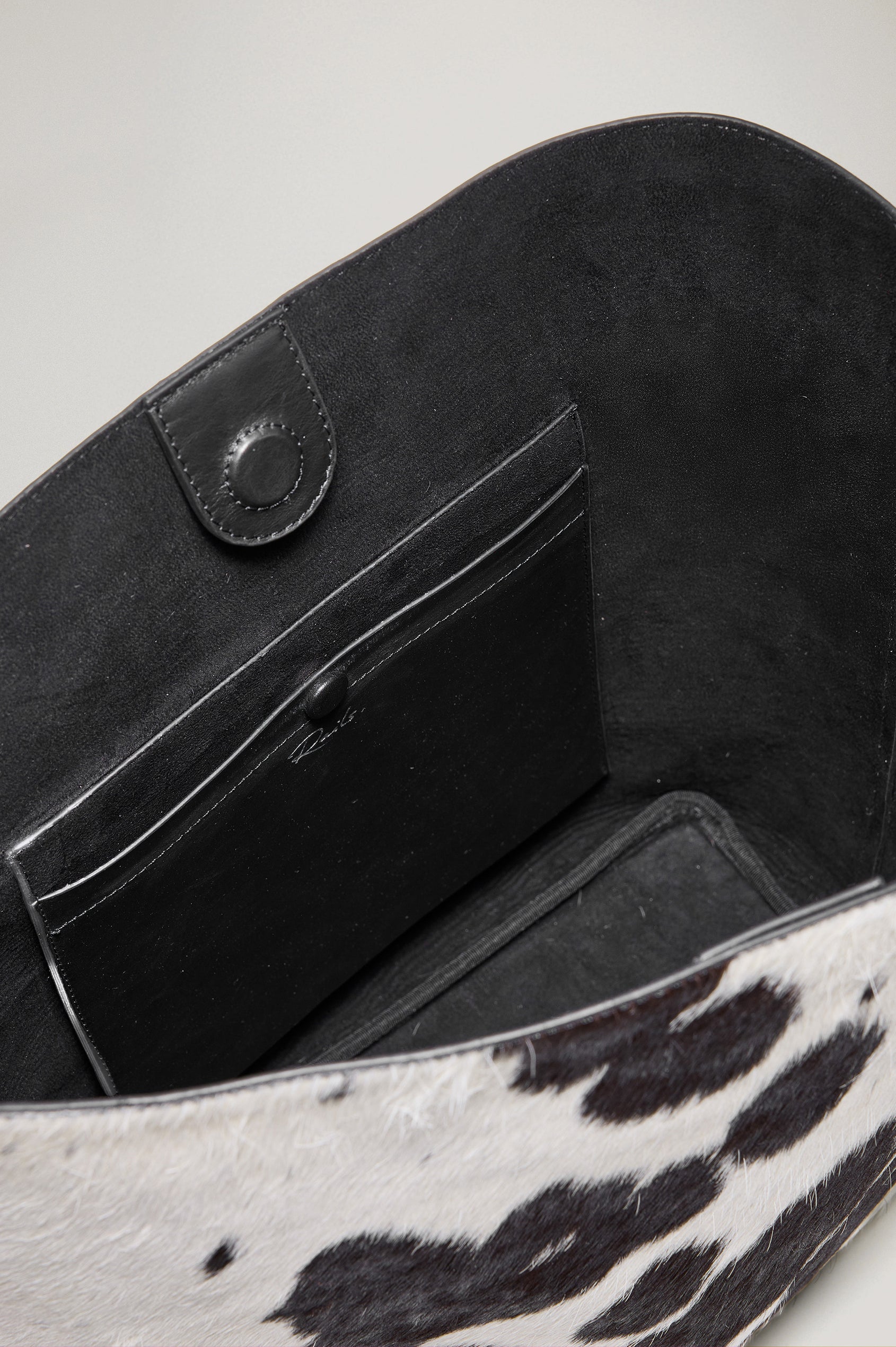 The Torino is a cow-print haircalf leather bucket bag, designed with an adjustable strap and polished silver oval buckle. Top view of interior featured.