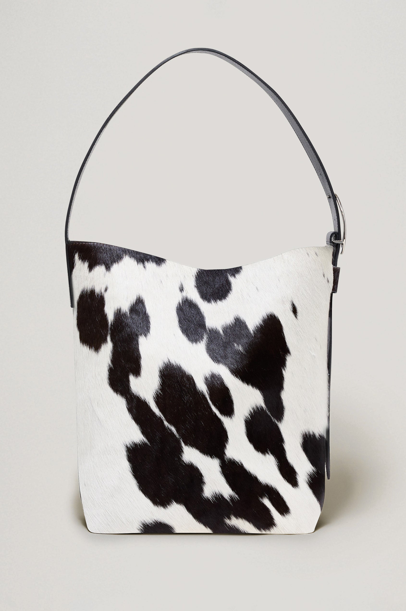 The Torino is a cow-print haircalf leather bucket bag, designed with an adjustable strap and polished silver oval buckle. Front view of bag featured.