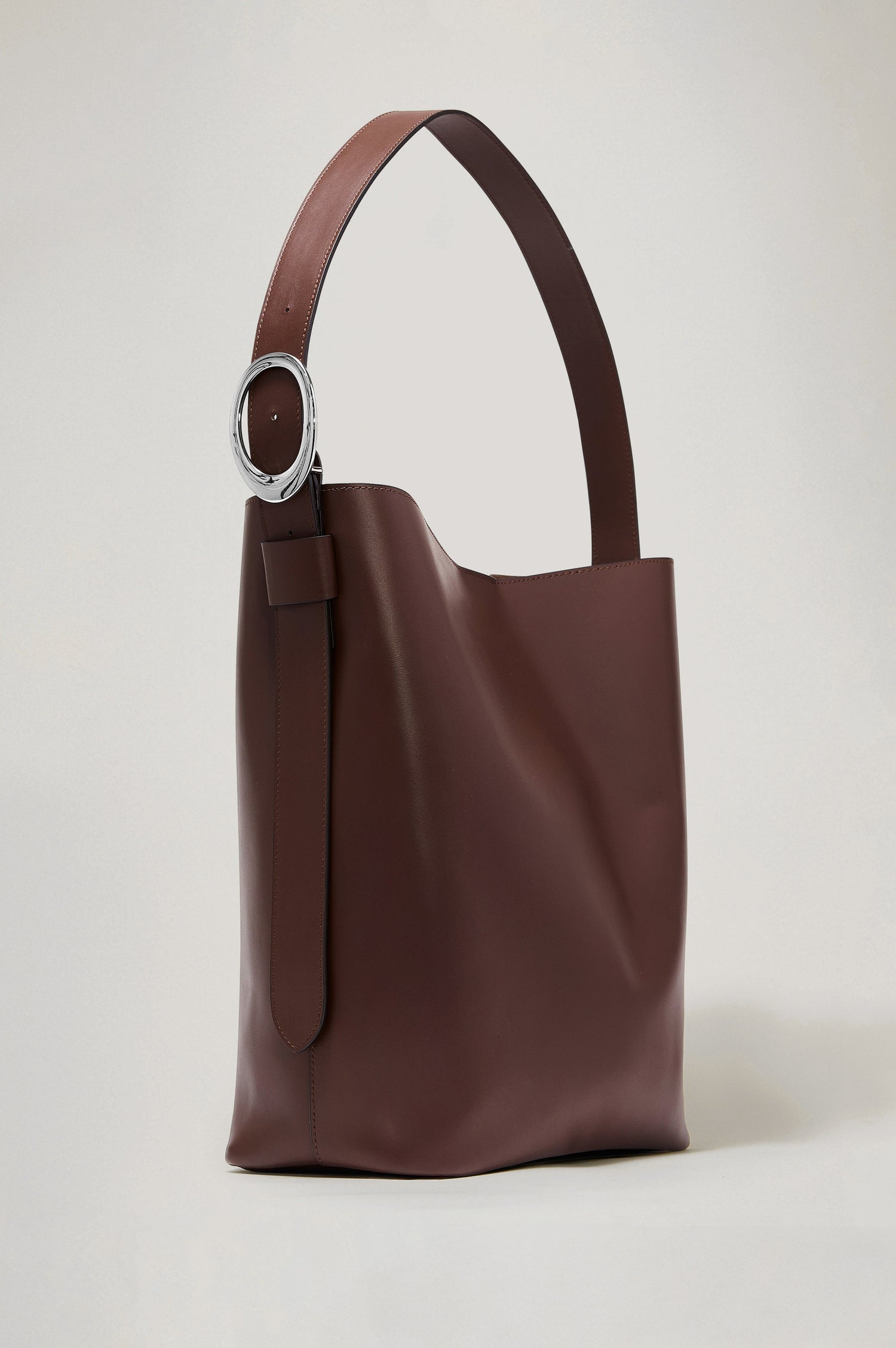The Torino is a soft leather bucket bag, designed with an adjustable strap and polished silver oval buckle, in espresso colorway. Front view featured.