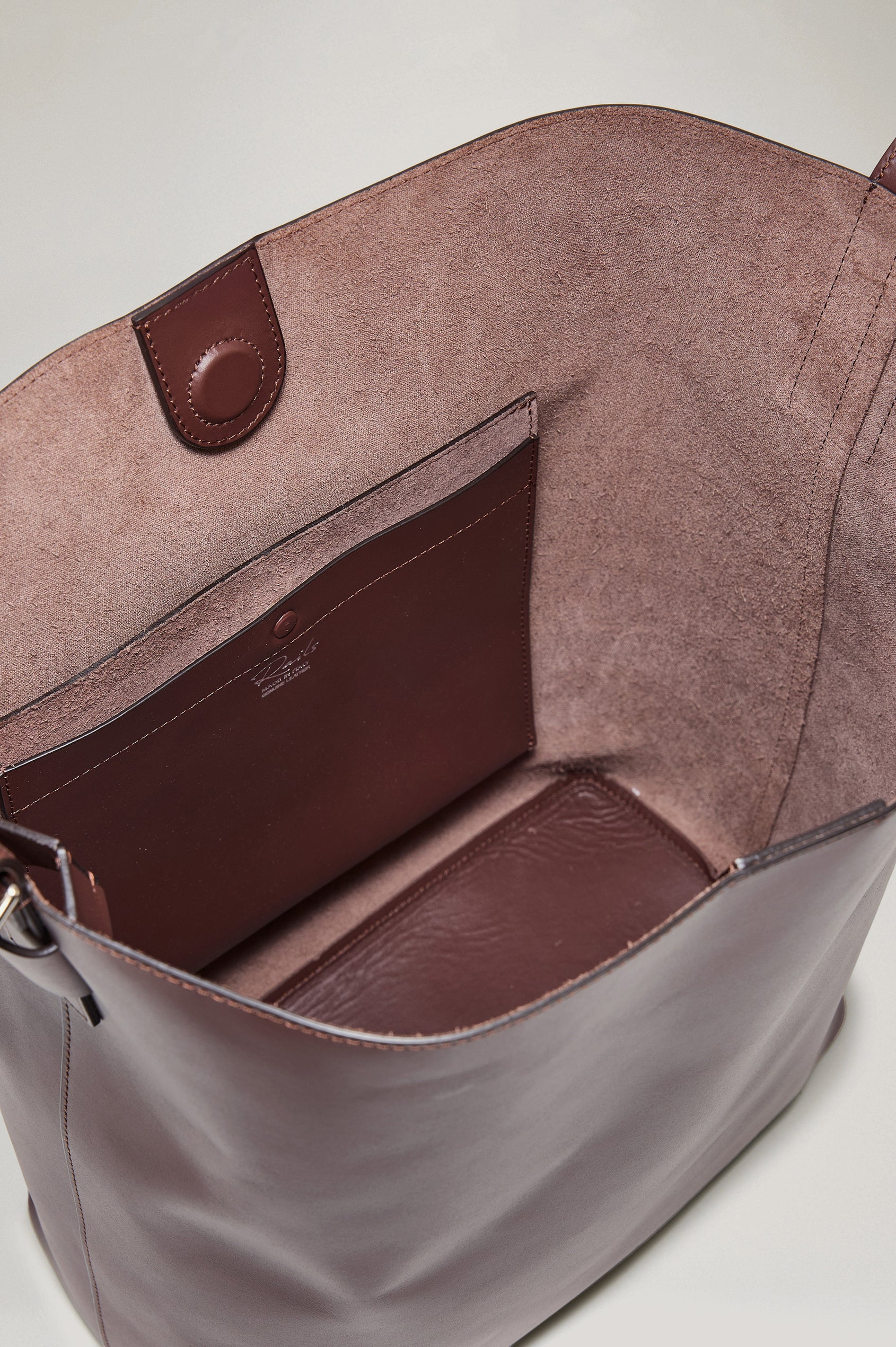 The Torino is a soft leather bucket bag, designed with an adjustable strap and polished silver oval buckle, in espresso colorway. Top view of interior featured.