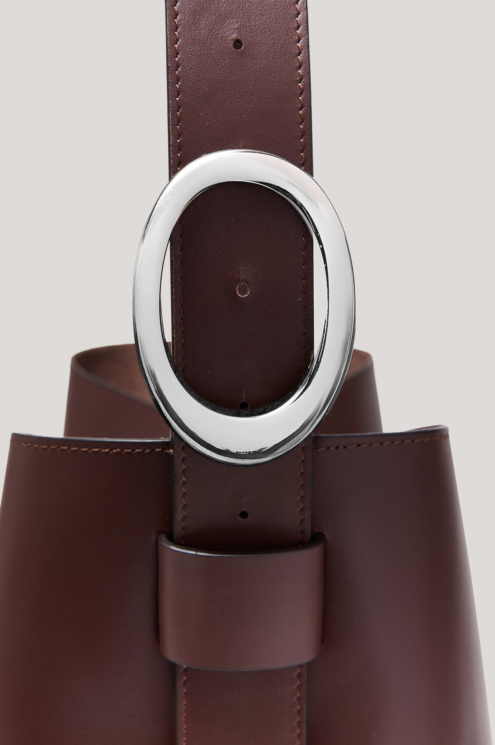 The Torino is a soft leather bucket bag, designed with an adjustable strap and polished silver oval buckle, in espresso colorway. Detailed view of buckle featured.