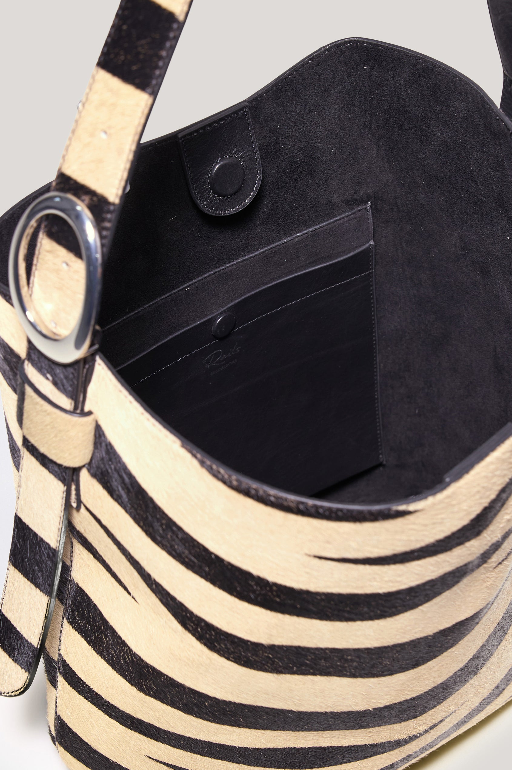 Torino Bucket Bag in Zebra Print Haircalf With Adjustable Strap and Polished Silver Oval Buckle, Microsuede Lining, Interior Magnetic Closure, Snap Button-Slip Pocket, and Subtle Branded Detailing in Zebra Haircalf Colorway - Top Interior View Featured
