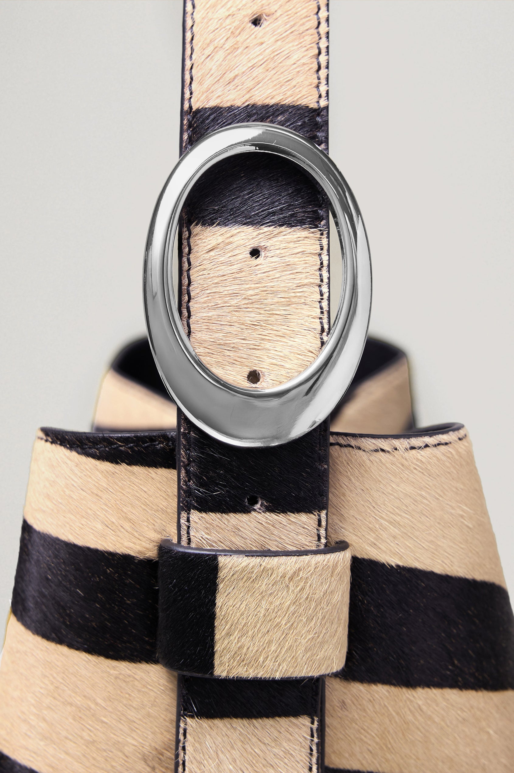 The Torino is a zebra-print haircalf leather bucket bag, designed with an adjustable strap and polished silver oval buckle. Detailed view of buckle featured.