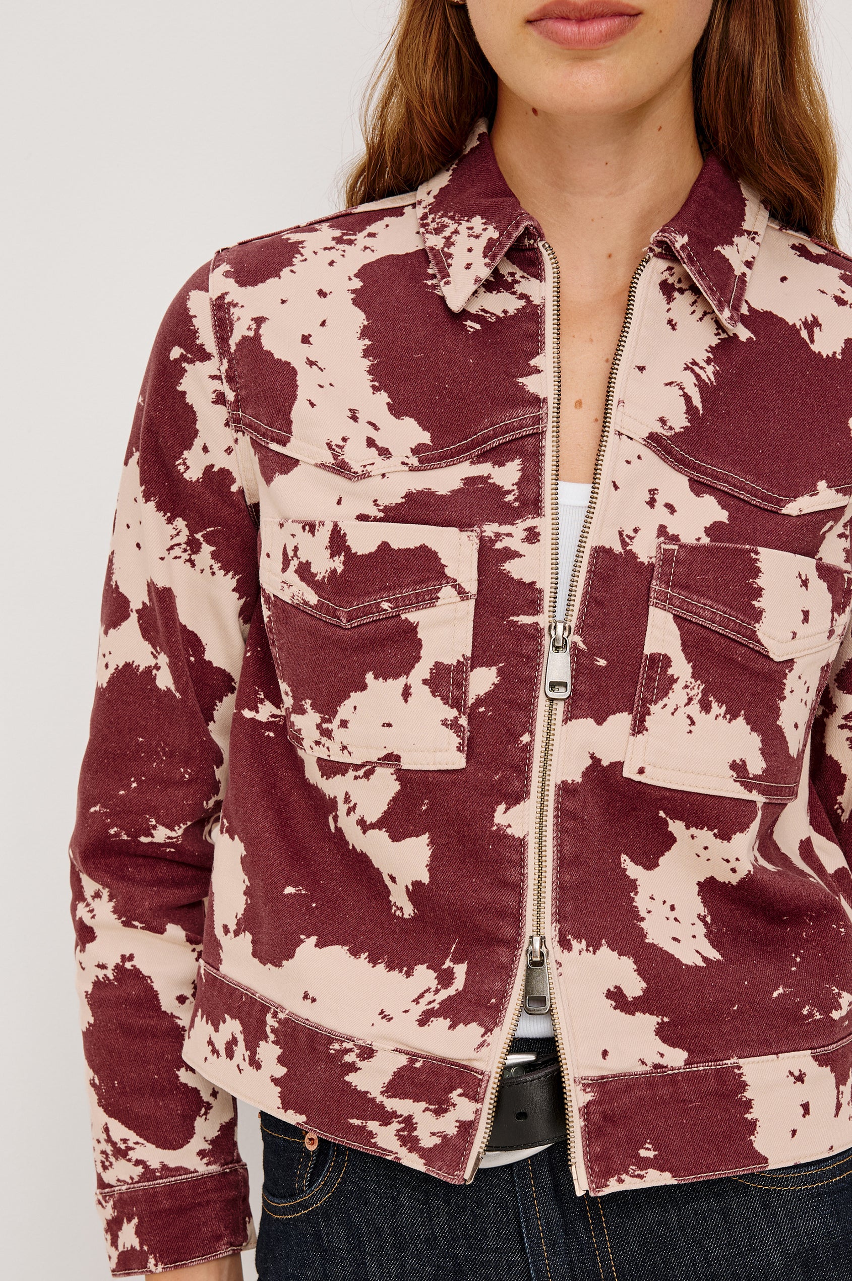 The Trabuco is a collared two-way zip front jacket with two chest pockets and a western style yoke in Cowgirl colorway - a red and beige cow print. Front detailed view featured on model.