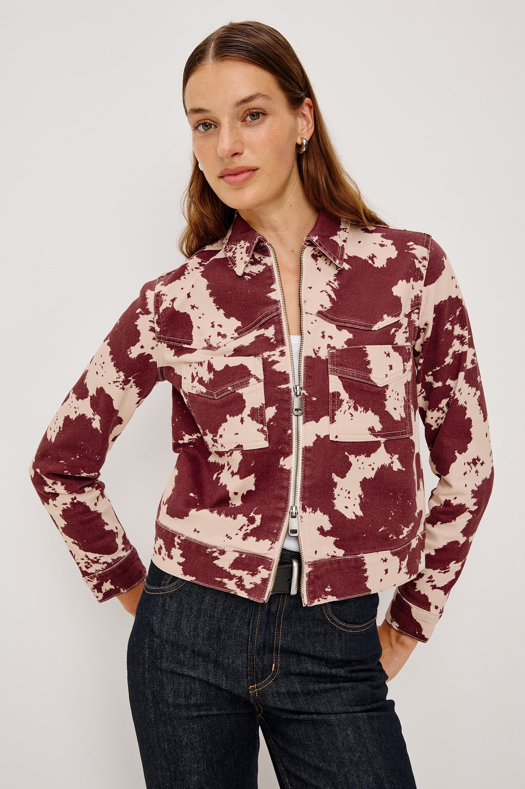 The Trabuco is a collared two-way zip front jacket with two chest pockets and a western style yoke in Cowgirl colorway - a red and beige cow print. Front view featured on model.
