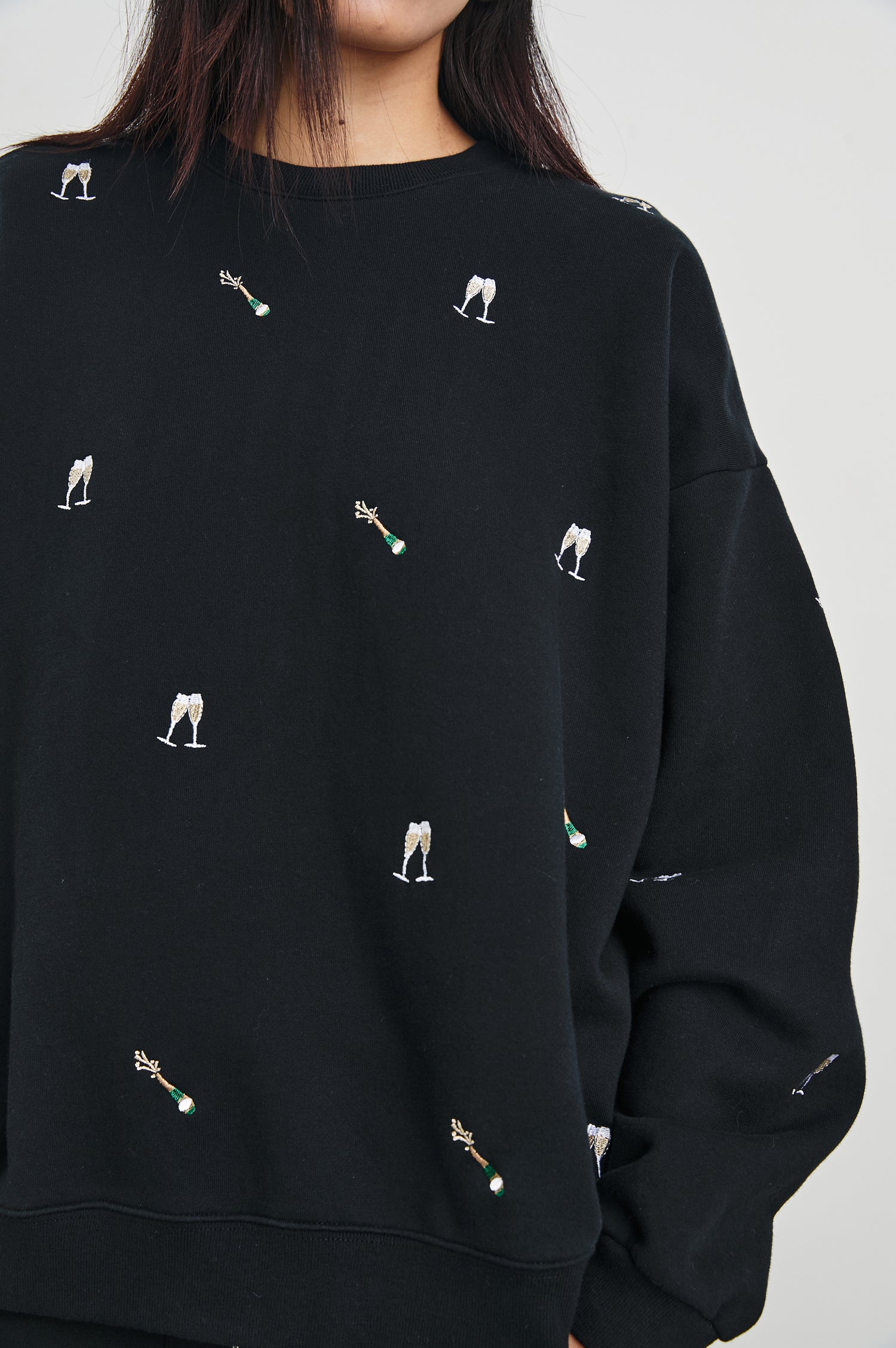 The Varsity Sweatshirt with a Crew Neck and embroidered Champagne Glasses in Black Champagne Embroidery Colorway, on Black - Front View Featured on Model 