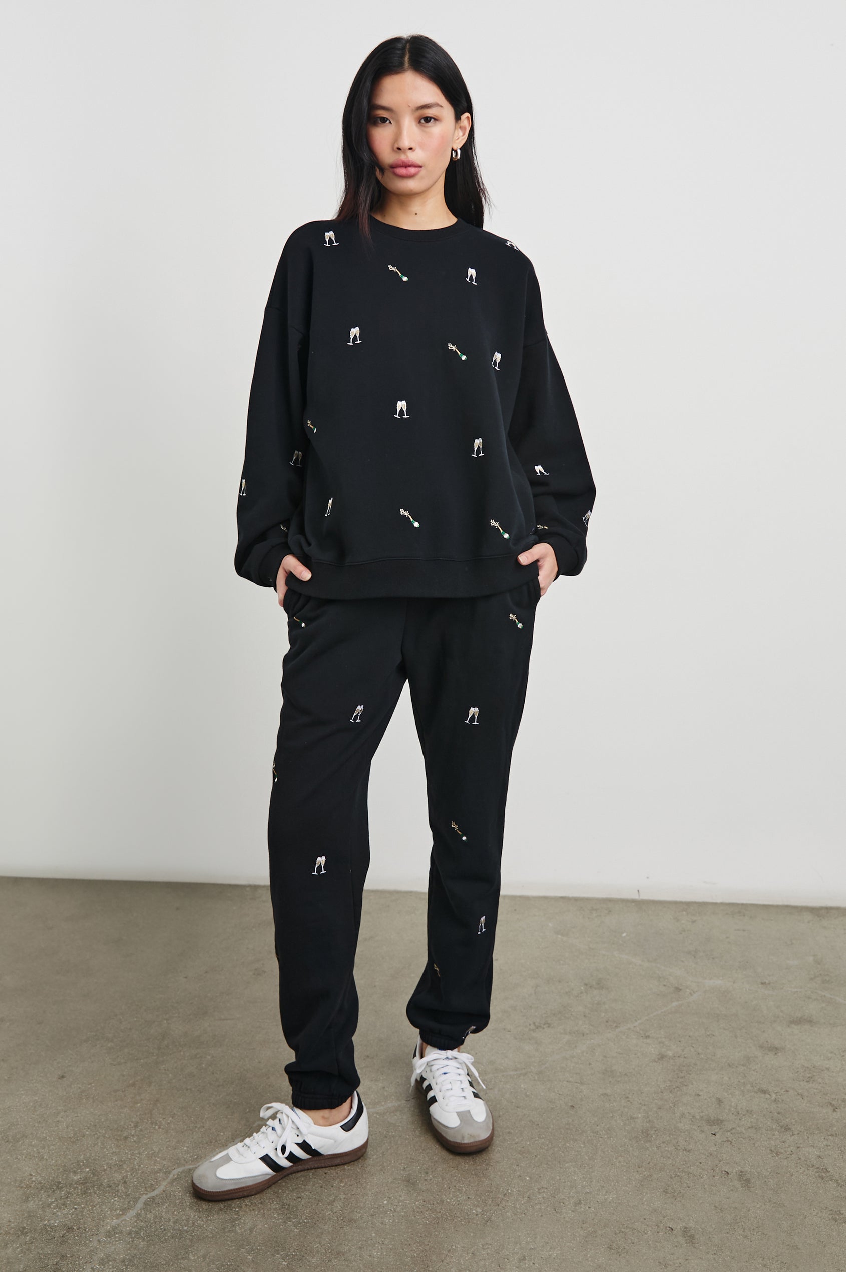 The Varsity Sweatshirt with a Crew Neck and embroidered Champagne Glasses in Black Champagne Embroidery Colorway, on Black - Front Full Body View Featured on Model 