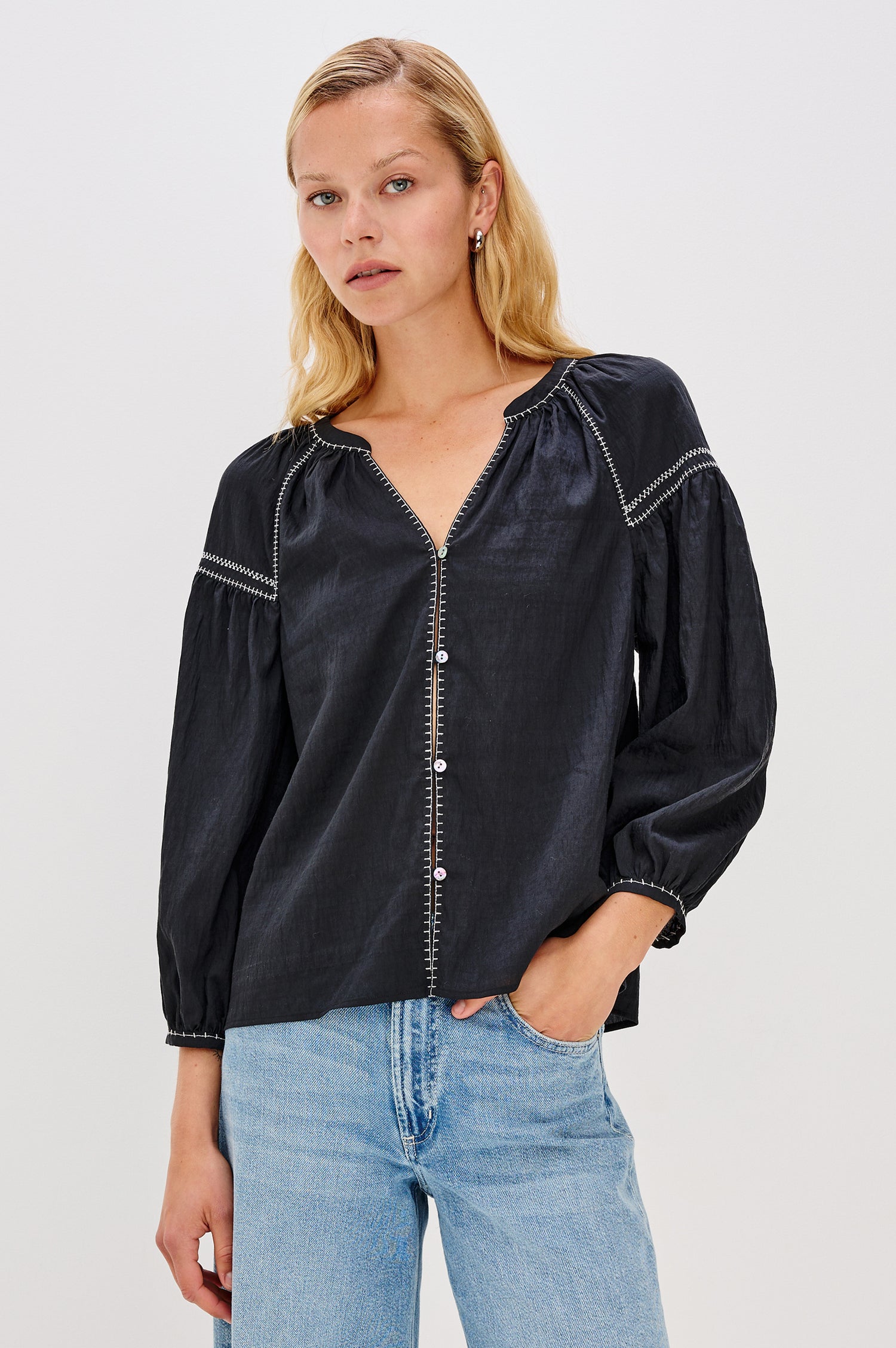 The Vasia is a long sleeve peasant top with a v-neck and button front, contrast white stitching and elastic at sleeve hems in Black colorway. Front view featured on model.