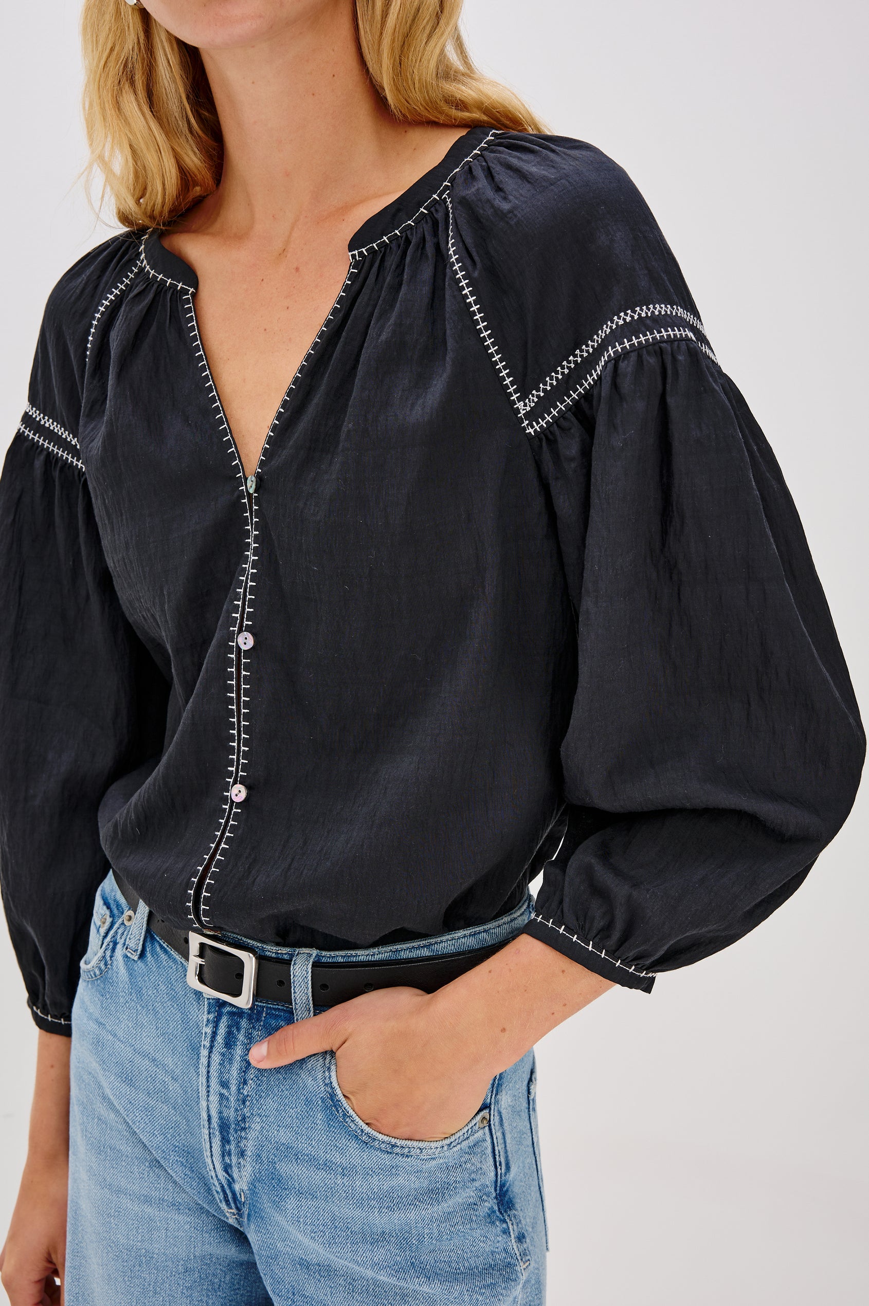 The Vasia is a long sleeve peasant top with a v-neck and button front, contrast white stitching and elastic at sleeve hems in Black colorway. Front detail view featured on model.