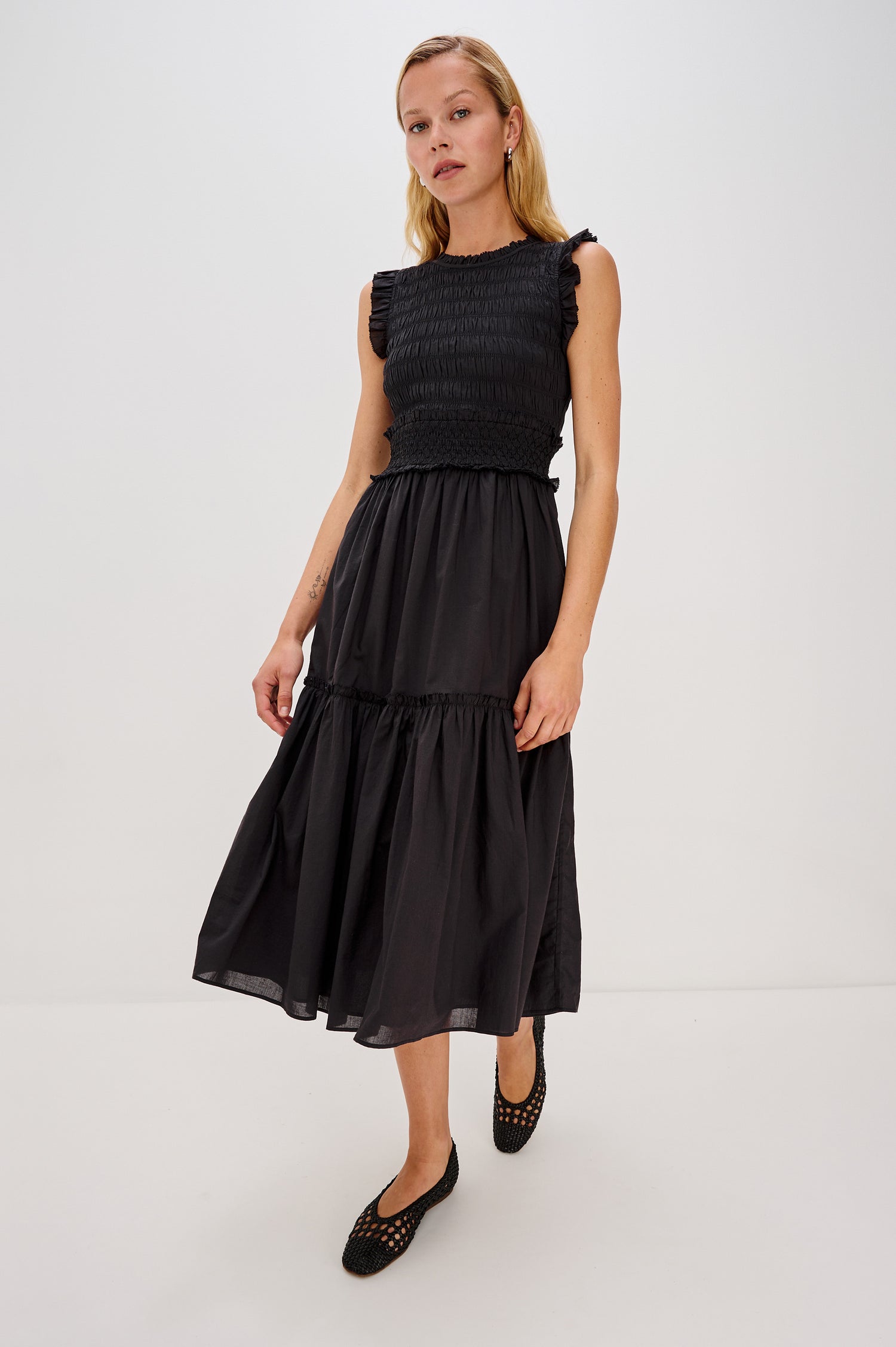Vivier is a crinkled cotton poplin maxi dress featuring a smocked, fitted bodice and waistband. The dress flows into a relaxed skirt with soft ruffled tiers, creating a breezy silhouette in Black Colorway - Full Body Front View Featured on Model