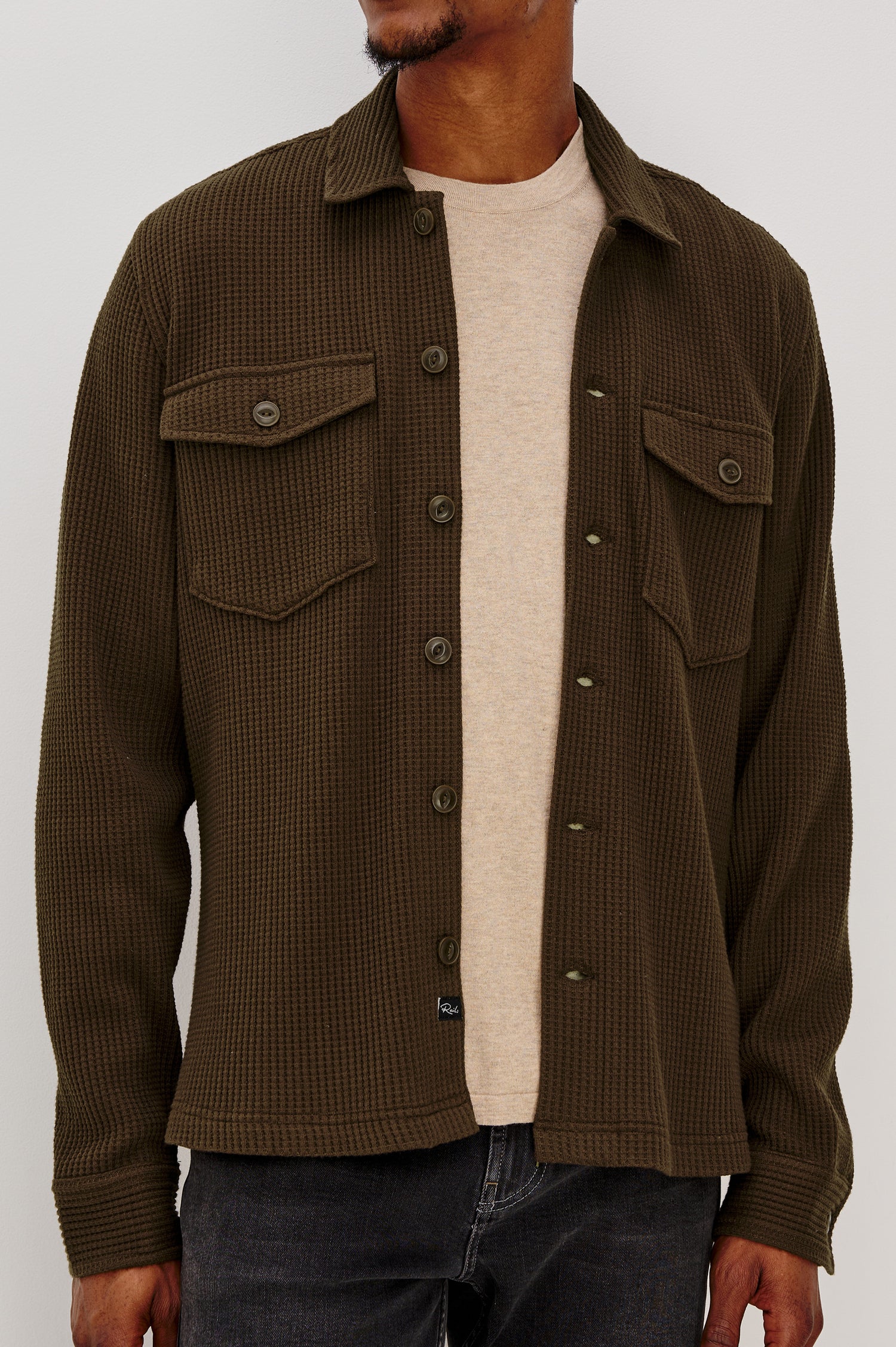 The Wells is a collared button front shirt jacket with contrast brown buttons and two chest pockets in Barley colorway. Front detail view featured on model.