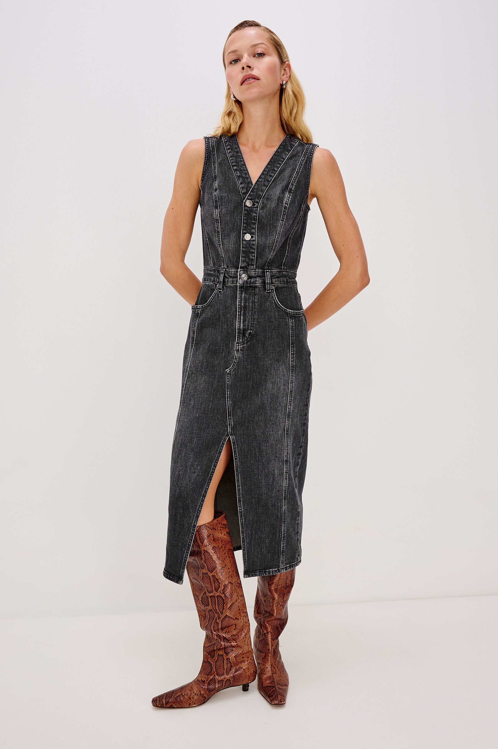Westwood Sleeveless Denim Midi Dress with Belt Loops, a Button and Zipper Closure for the Skirt and Button Closure on the Bodice, a V neck, a Front Center Thigh Slit, Two Front Pockets  and Two Back Patch Pockets in Black Pearl Colorway, a washed black- Front Full Body View Featured on Model