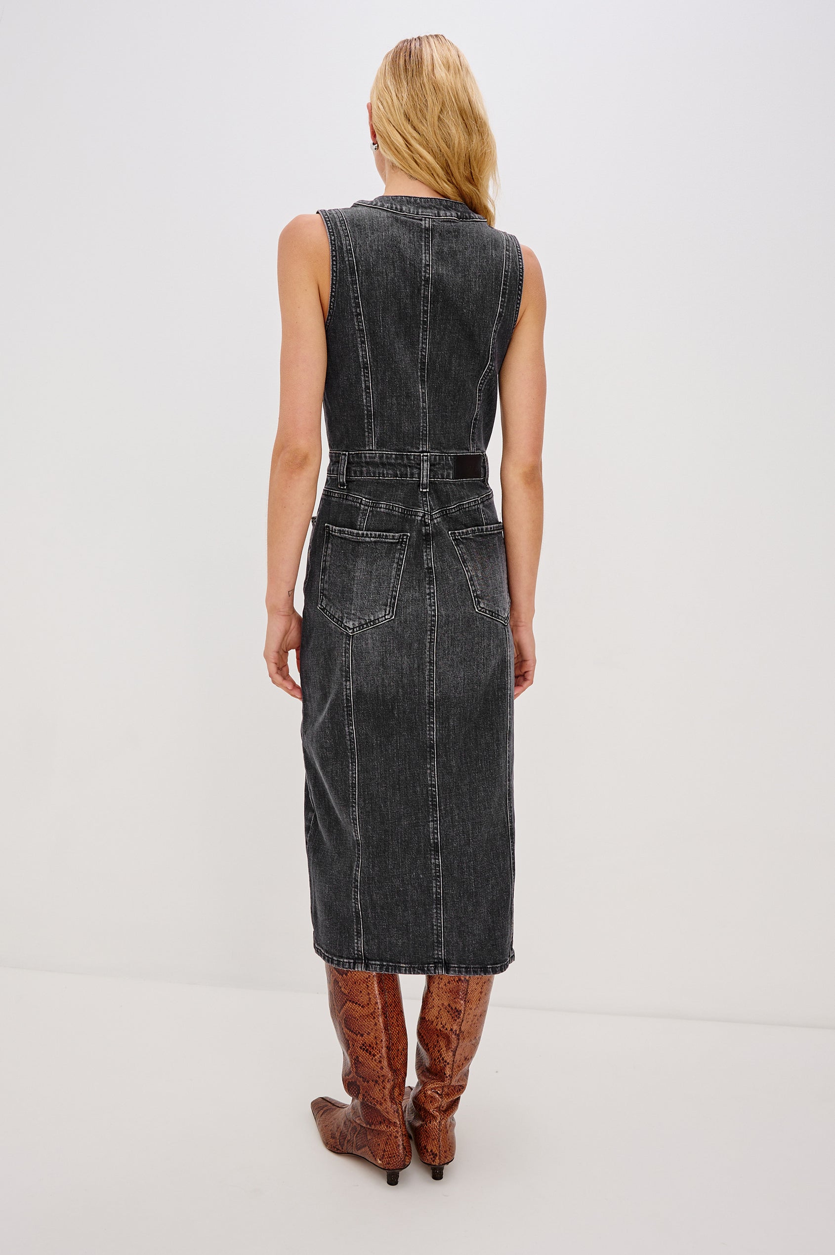 Westwood Sleeveless Denim Midi Dress with Belt Loops, a Button and Zipper Closure for the Skirt and Button Closure on the Bodice, a V neck, a Front Center Thigh Slit, Two Front Pockets  and Two Back Patch Pockets in Black Pearl Colorway, a washed black- Back Full Body View Featured on Model