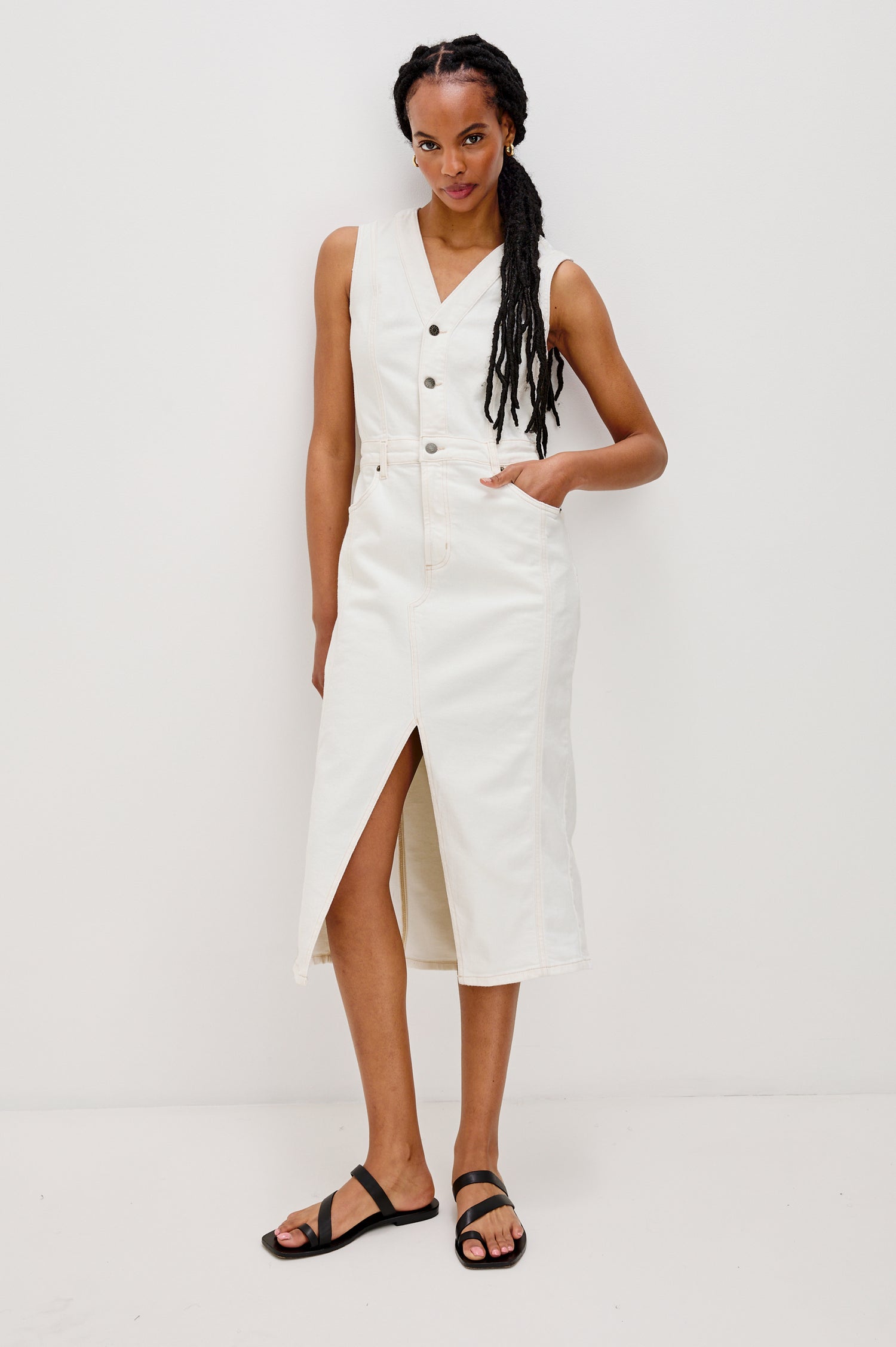 Westwood Sleeveless Denim Midi Dress with Belt Loops, a Button and Zipper Closure for the Skirt and Button Closure on the Bodice, a V neck, a Front Center Thigh Slit, Two Front Pockets  and Two Back Patch Pockets in Vintage Ecru Colorway - Full body Front View Featured on Model
