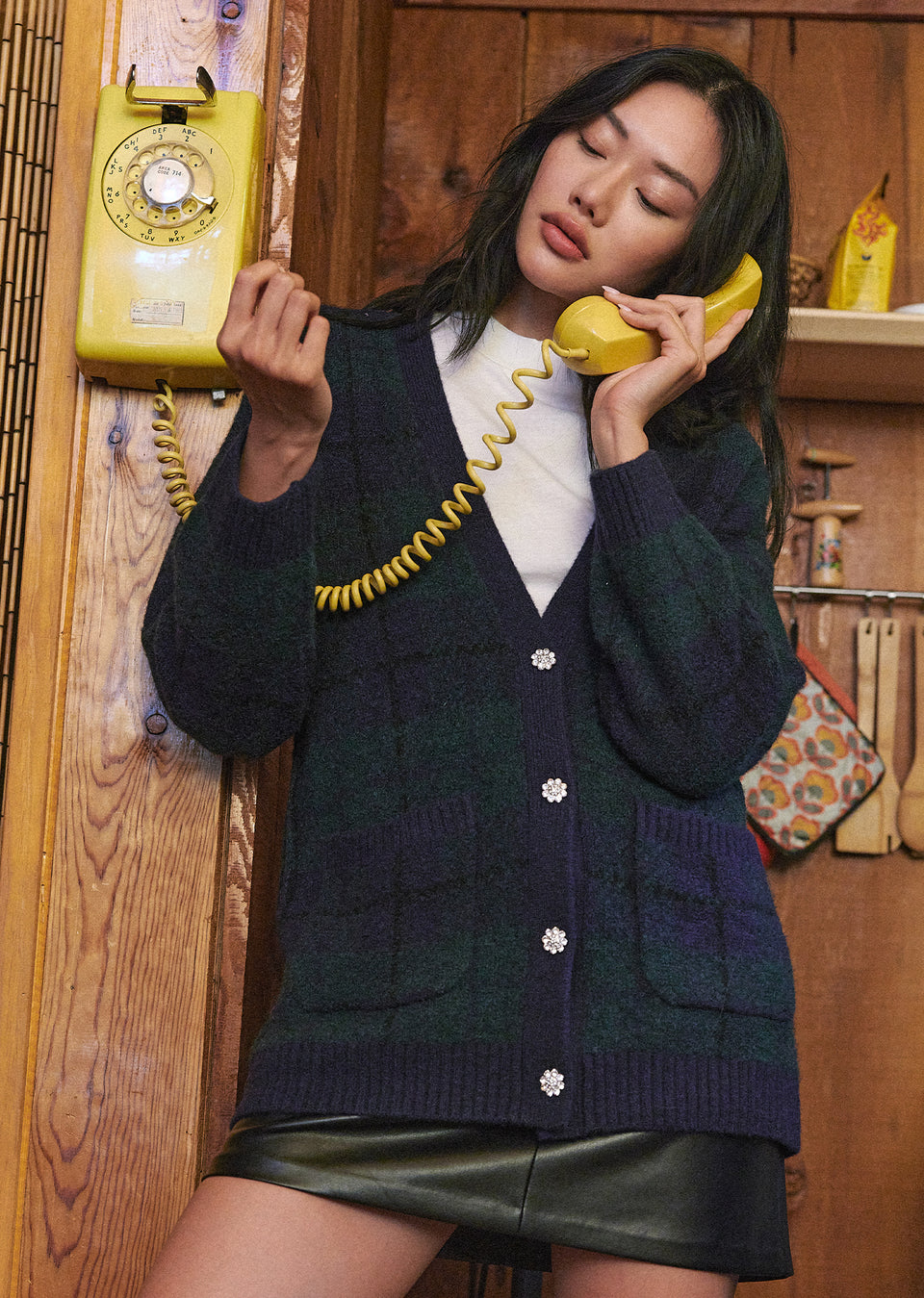 FRONT EDITORIAL IMAGE OF MODEL ON THE PHONE WEARING RUNI CARDIGAN IN NAVY TARTAN AND PRIM SKIRT IN BLACK