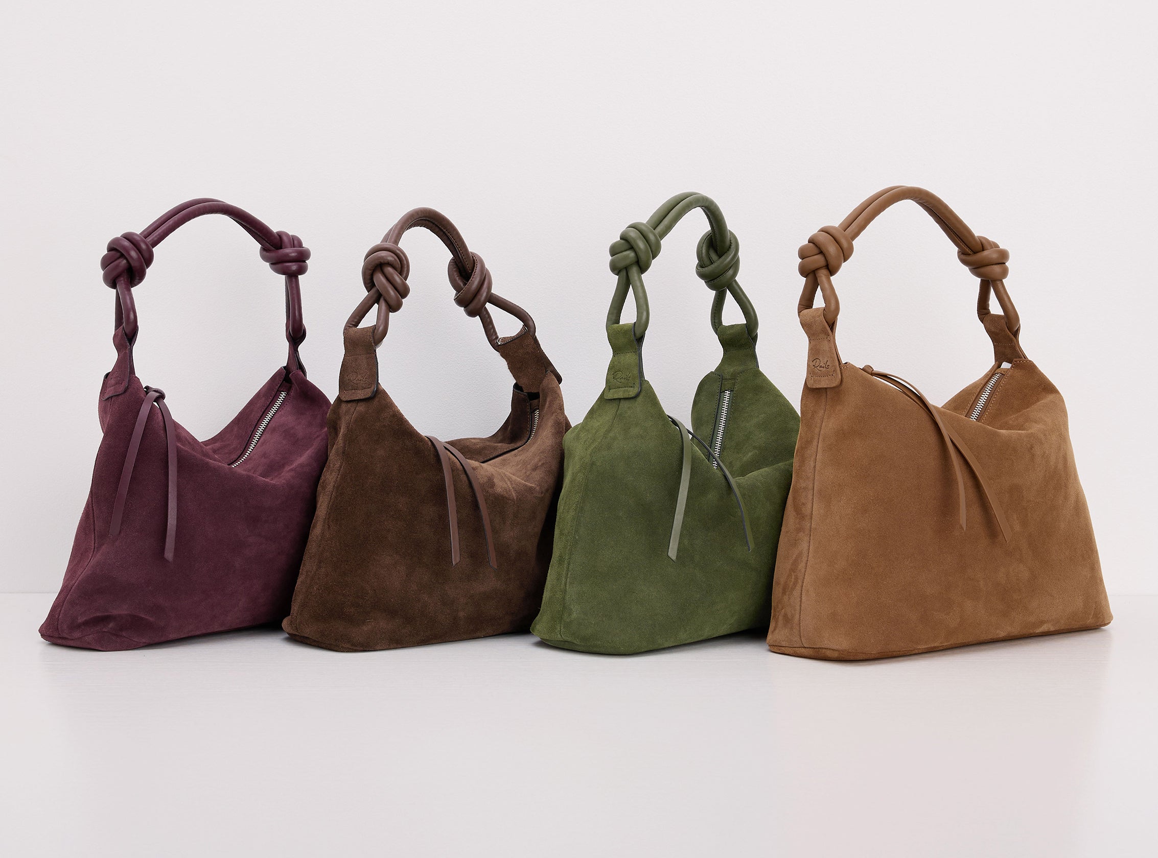 Four suede shoulder bags in plum, taupe, olive green, and camel brown, arranged in a row on a clean white background.